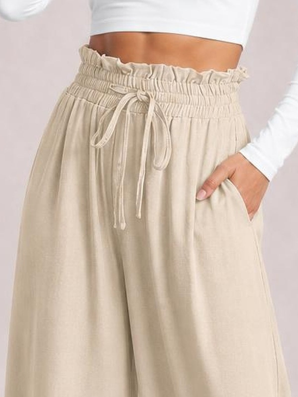 Model wears beige drawstring wide leg pants with a gathered elastic waistband, flowing silhouette, and side pockets, with one hand tucked inside.