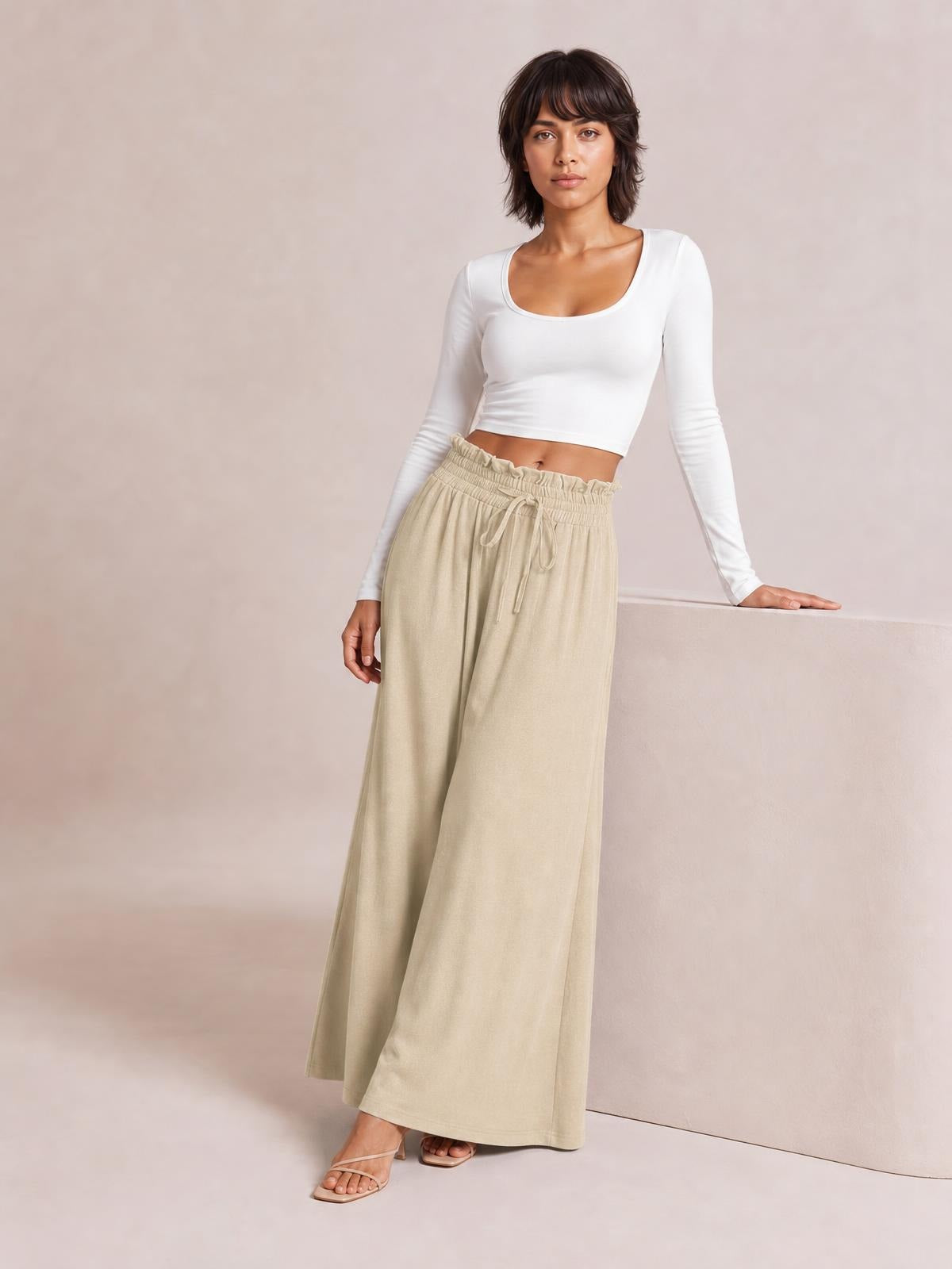 A model poses in flowy beige drawstring wide leg pants with a gathered elastic waist and relaxed full-length silhouette.