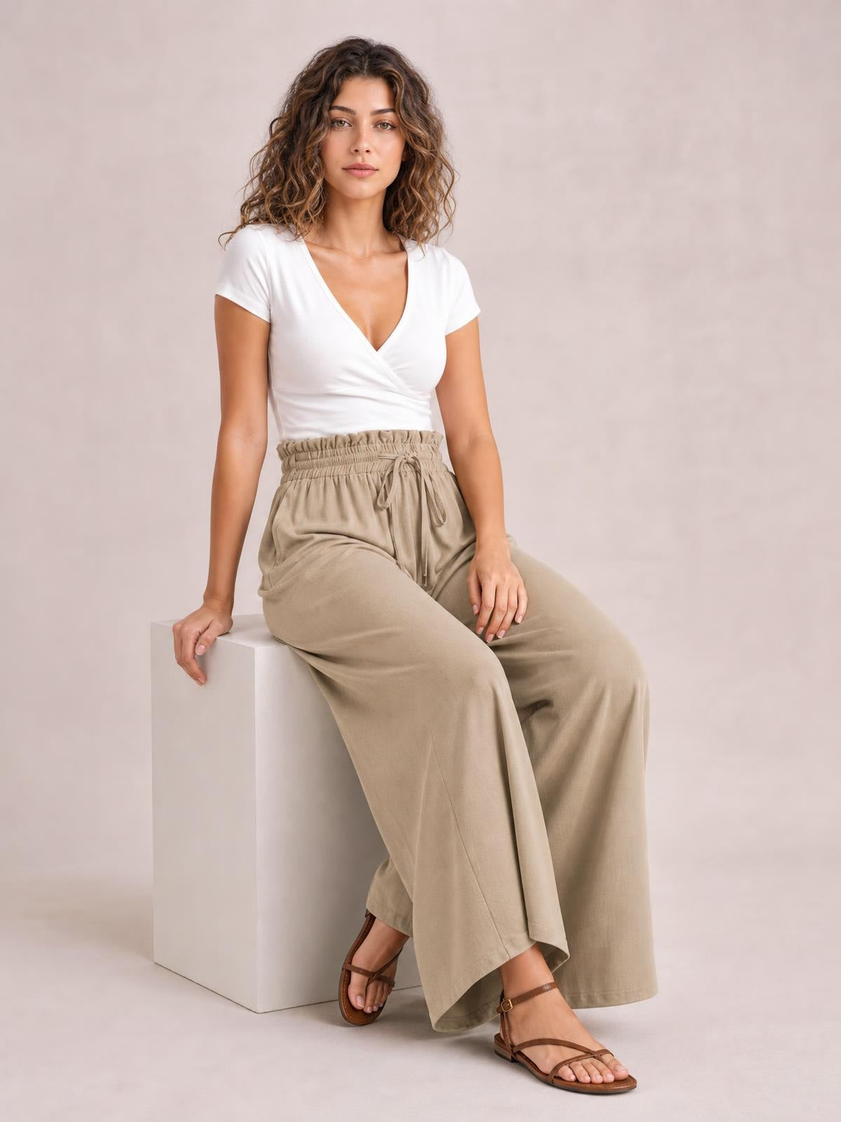 Model seated in beige drawstring wide-leg pants with a relaxed, flowy silhouette, elastic waist, front tie, and visible side pockets.