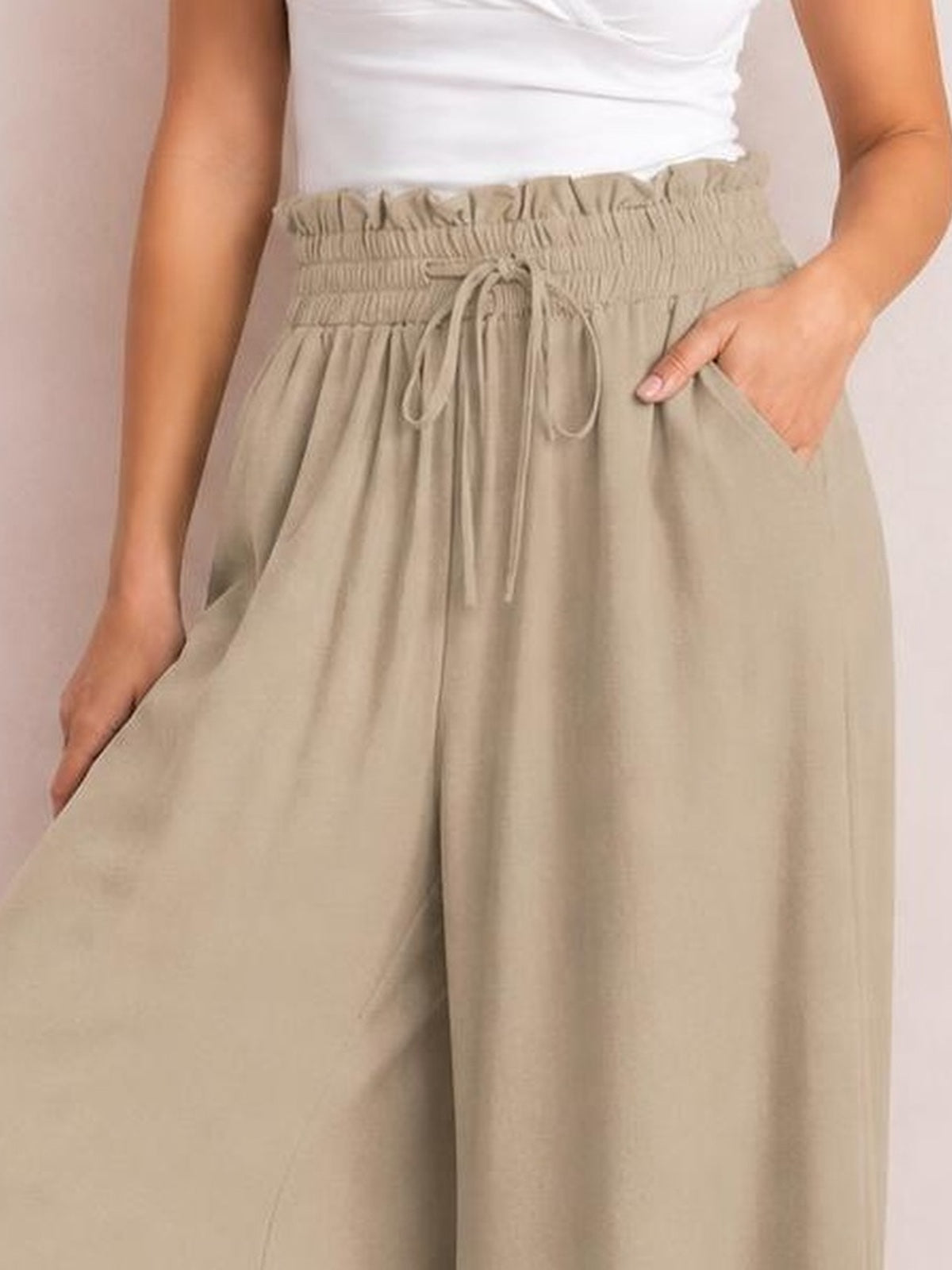 Model wears beige drawstring wide-leg pants with a gathered elastic waistband, relaxed flowy silhouette, and side pockets, one hand tucked inside.