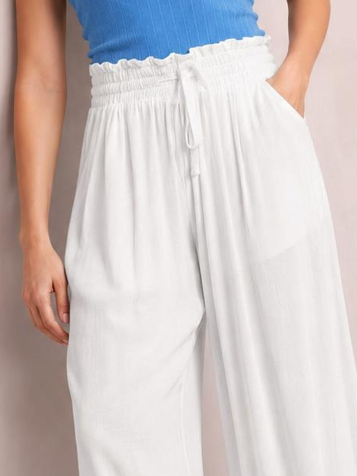 Model wearing white drawstring wide-leg pants with a smocked elastic waist, front tie, side pockets, and a loose flowy silhouette.
