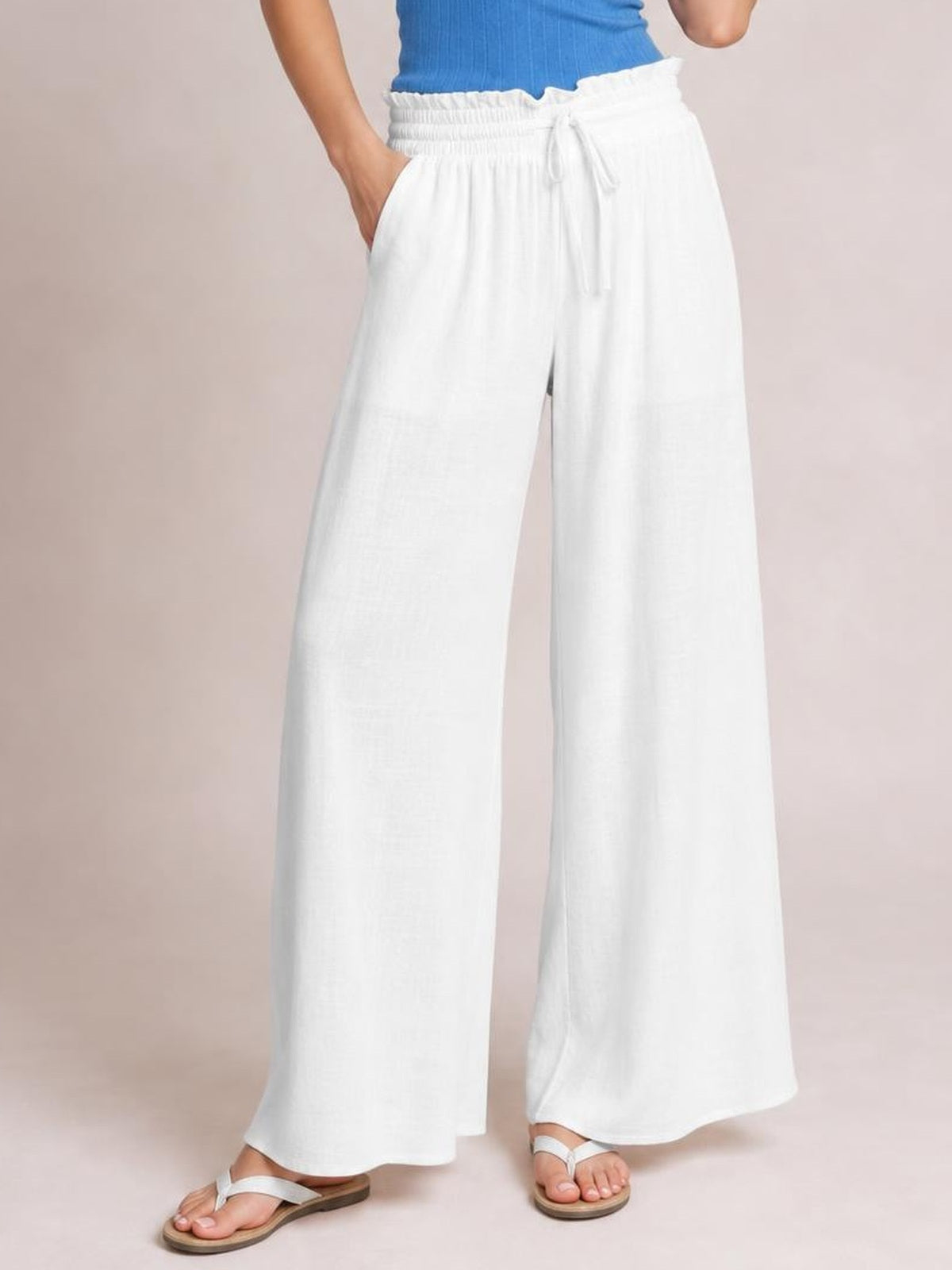Model wearing white drawstring wide leg pants with side pockets, a gathered elastic waist, and a flowy full-length silhouette.