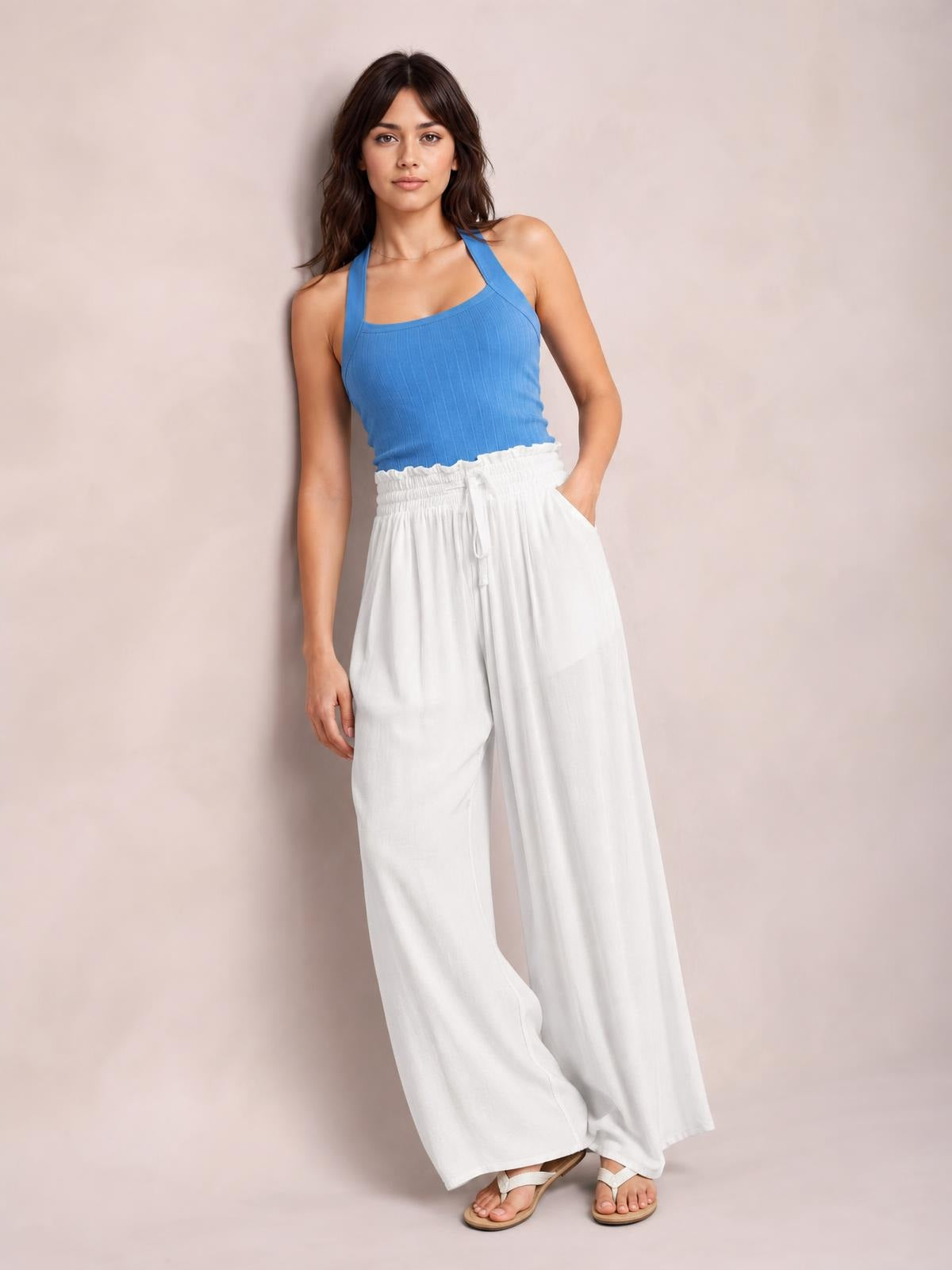 Model poses in white drawstring wide leg pants with a gathered waistband, flowing full-length silhouette, and side pockets.