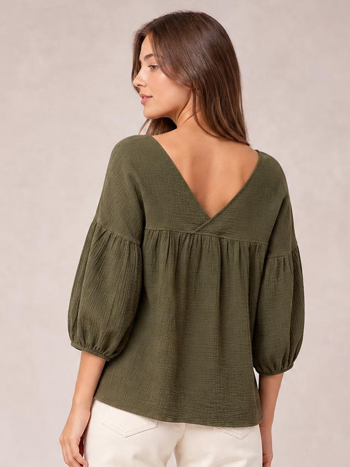 A model turned away wears an olive green solid blouse with a deep V-neck back, dropped shoulders, gathered long sleeves, and a relaxed long silhouette.