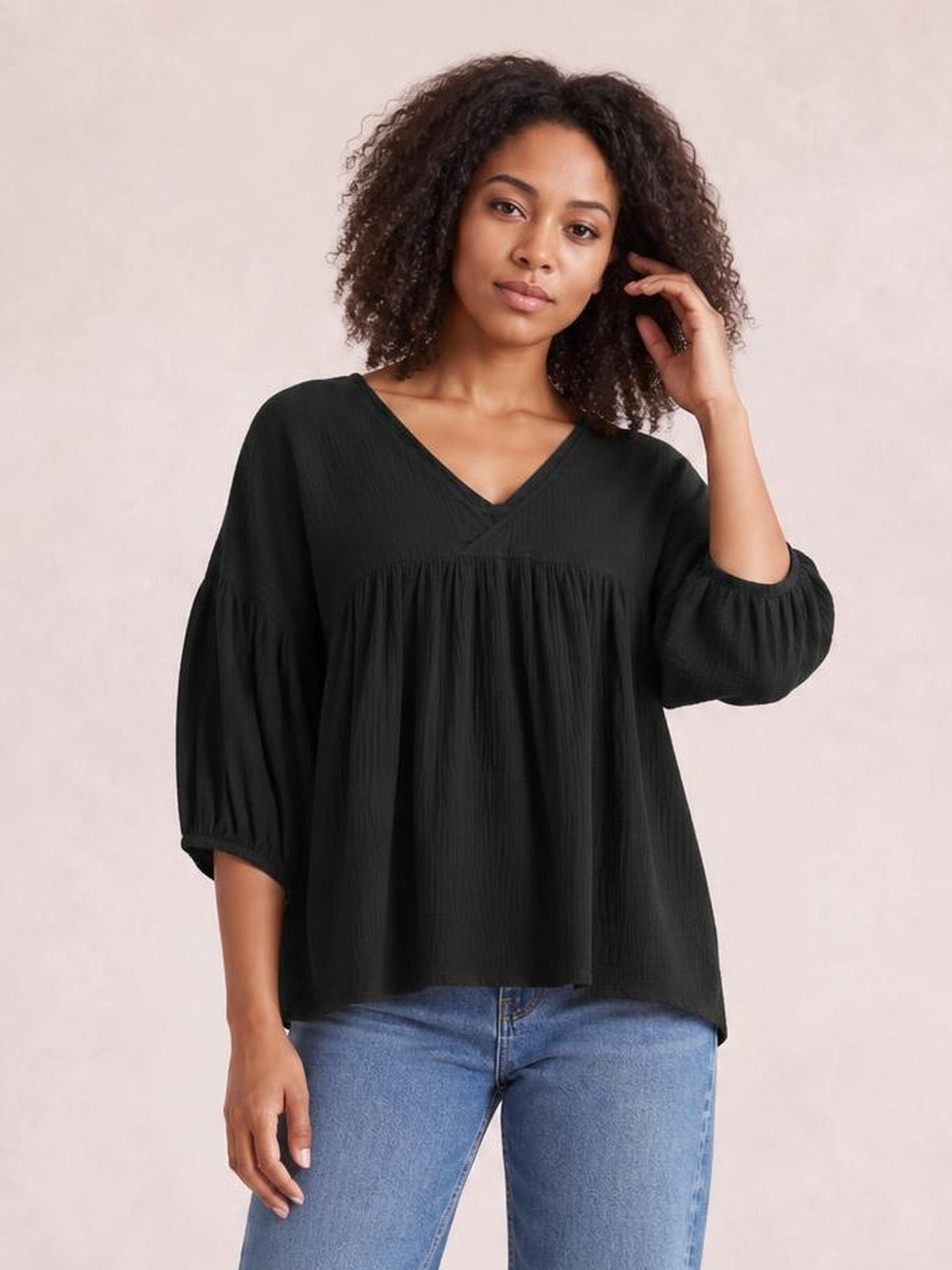 Model poses in a black dropped-shoulder V-neck blouse with long gathered sleeves, a relaxed loose silhouette, and a long flowing hem.