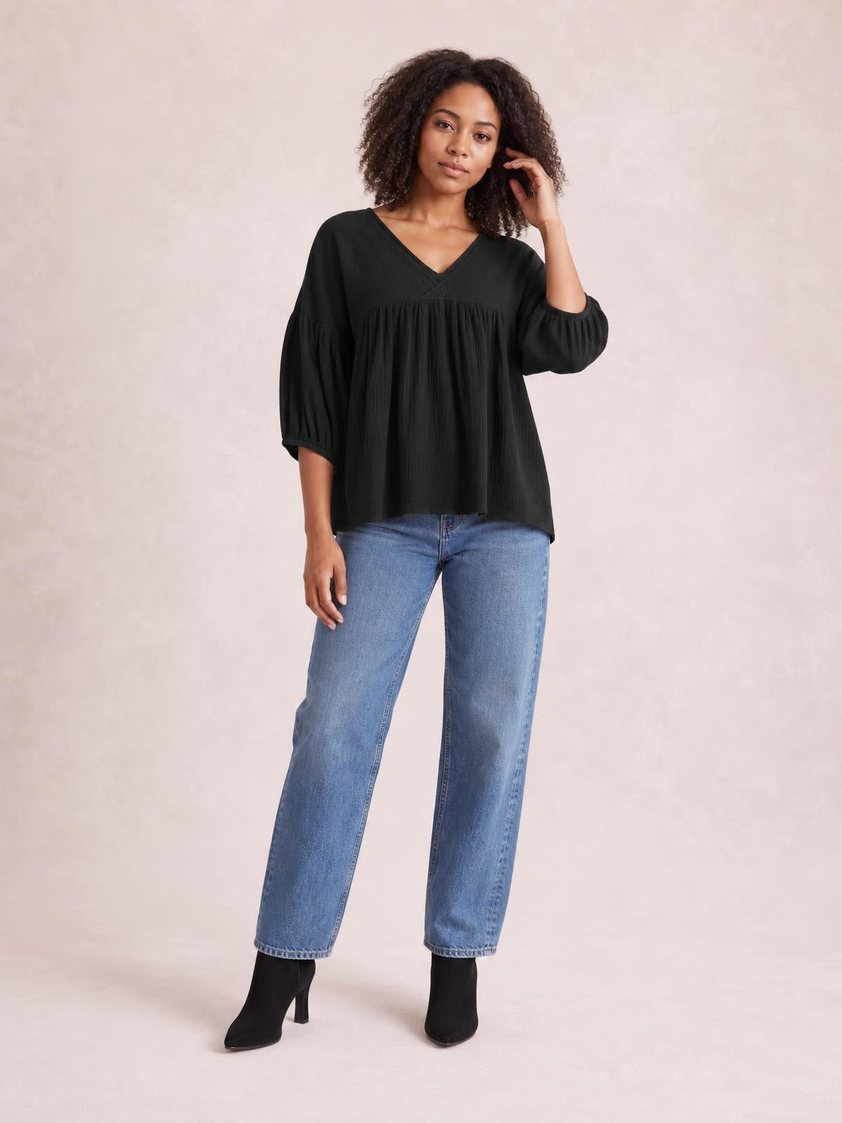 Model wearing a solid black dropped-shoulder V-neck blouse with long balloon sleeves, gathered seam detailing, and a loose long silhouette.