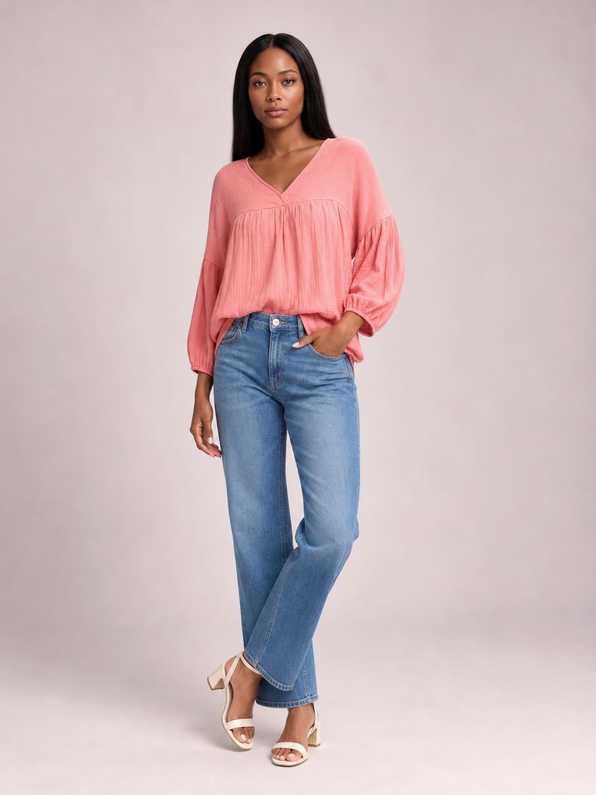 Model poses in a solid pink dropped-shoulder V-neck blouse with long sleeves, a relaxed silhouette, and gathered detailing across the front.