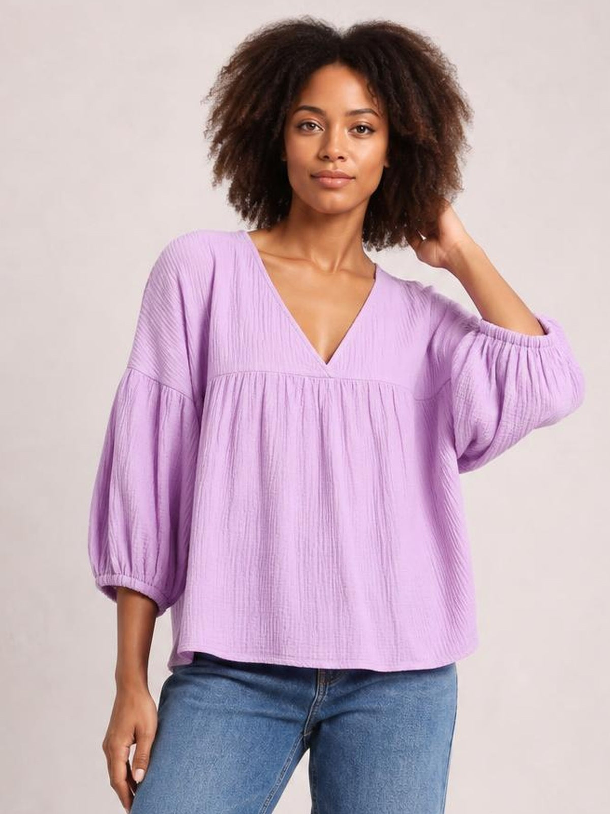 A model wears a solid lavender dropped-shoulder V-neck blouse with a loose silhouette, gathered lower panel, long balloon sleeves, and elastic cuffs.