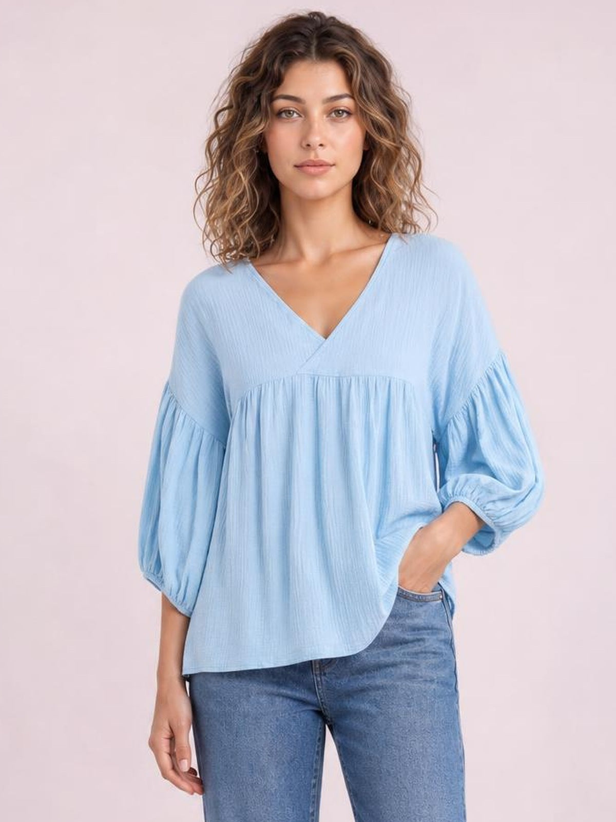 A model wears a light blue solid V-neck blouse with dropped shoulders, long gathered sleeves, elastic cuffs, and a relaxed, flowing silhouette.