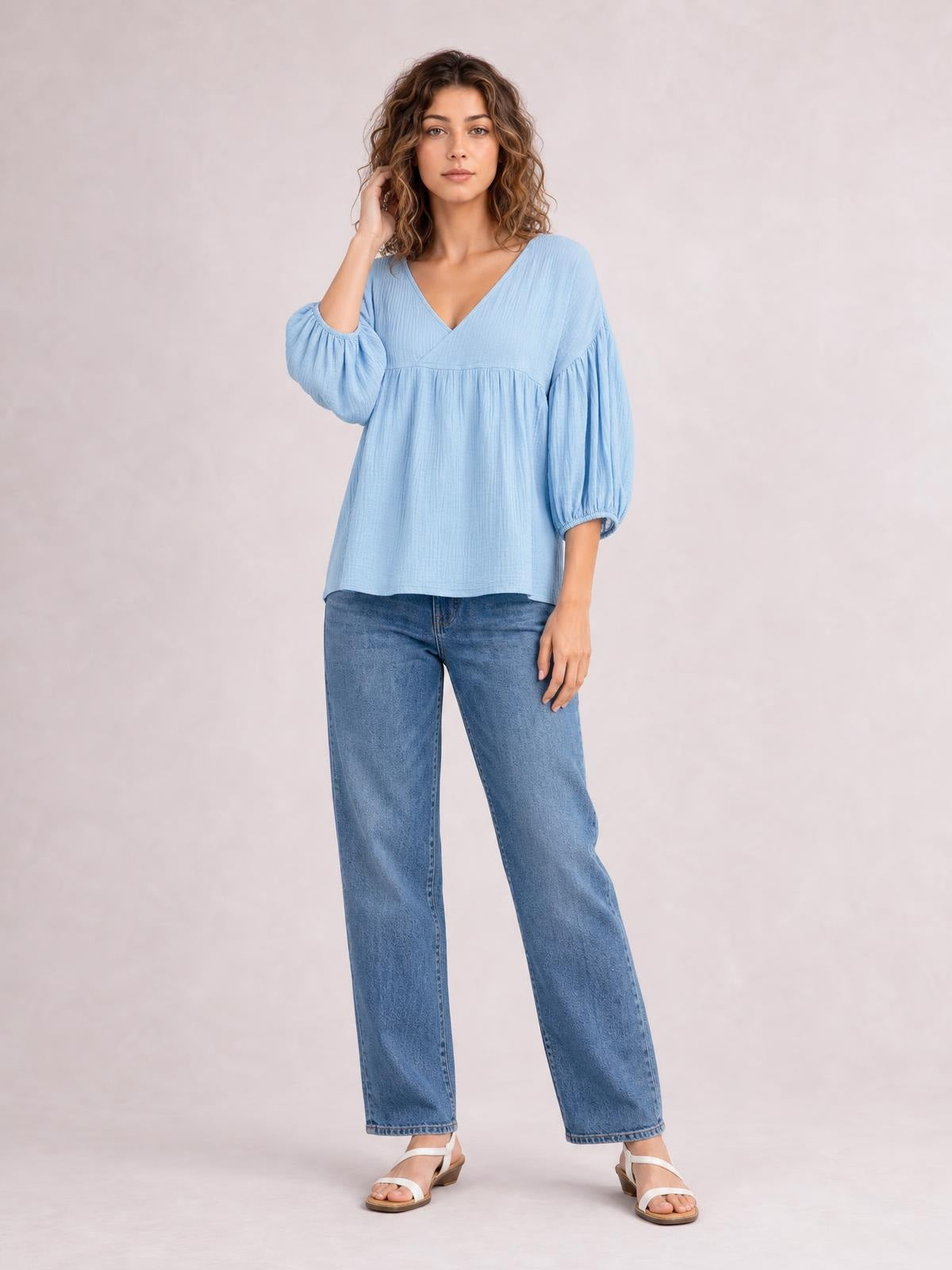 Model poses in a light blue dropped shoulder V-neck blouse with long gathered sleeves, a relaxed long silhouette, and a gathered seam across the bodice.