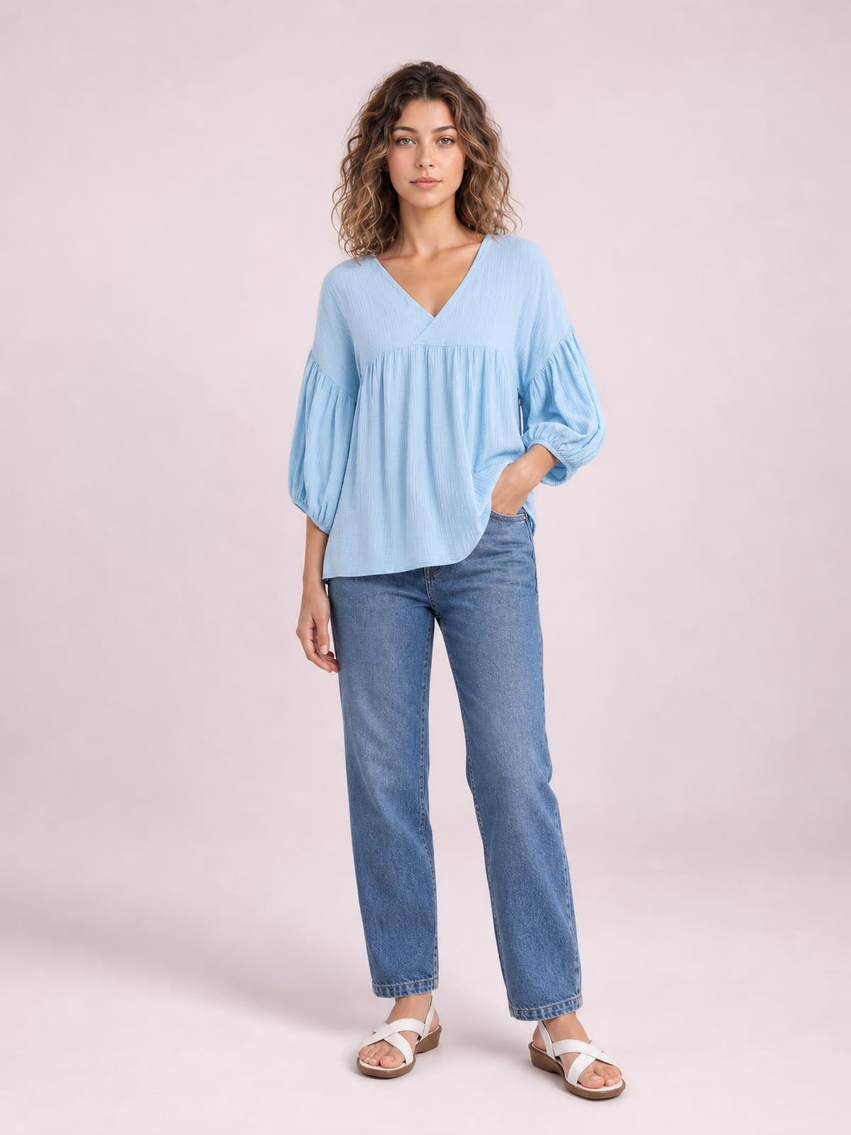 Model wears a solid light blue dropped-shoulder V-neck blouse with long gathered sleeves, a loose flowing silhouette, and a softly curved hem.