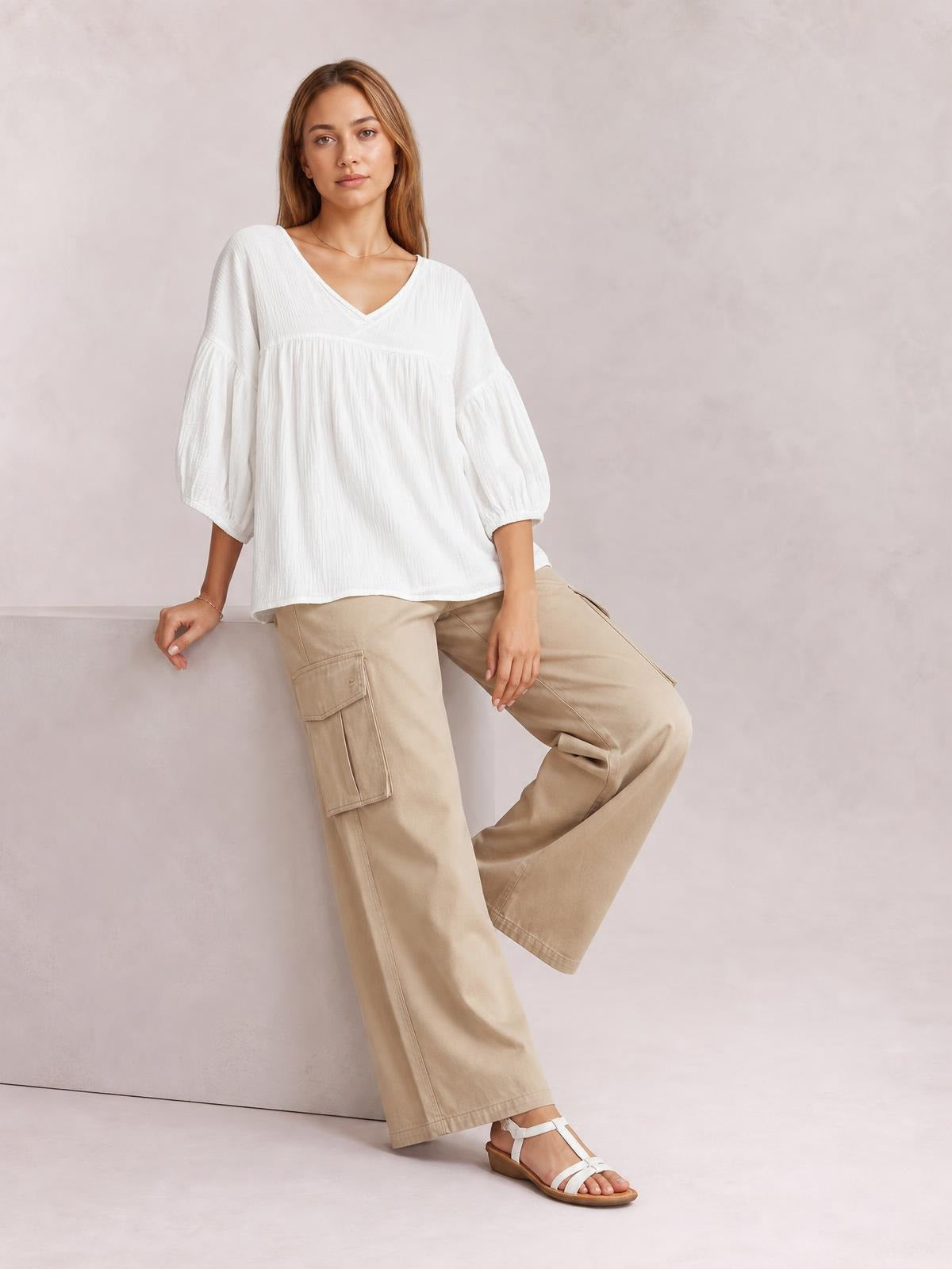 A model leans in a solid white dropped-shoulder blouse with a V-neck, gathered yoke, loose silhouette, and voluminous long sleeves.