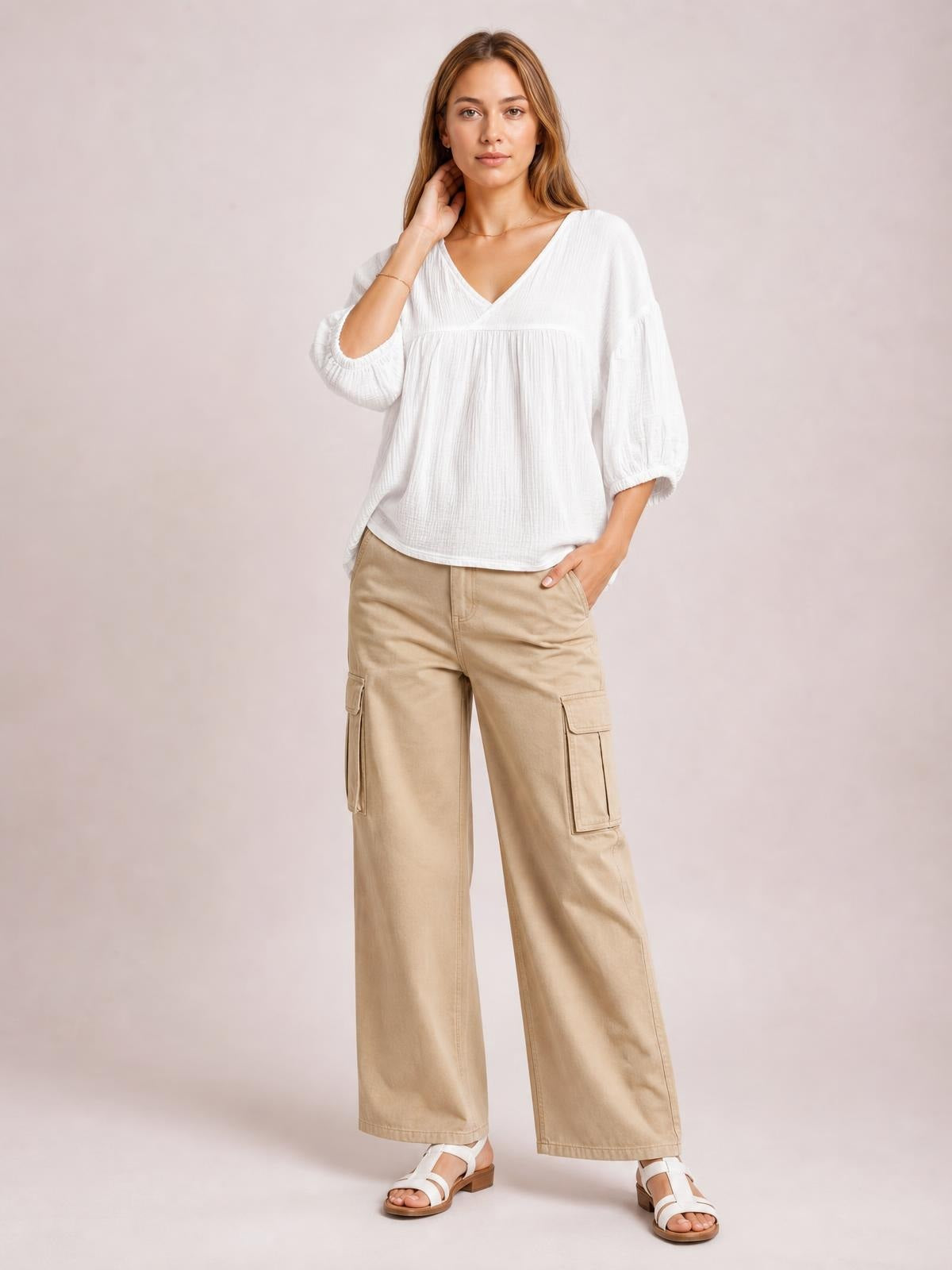 Model poses in a solid white dropped shoulder V-neck blouse with long sleeves, gathered yoke, relaxed silhouette, and gently curved hem.