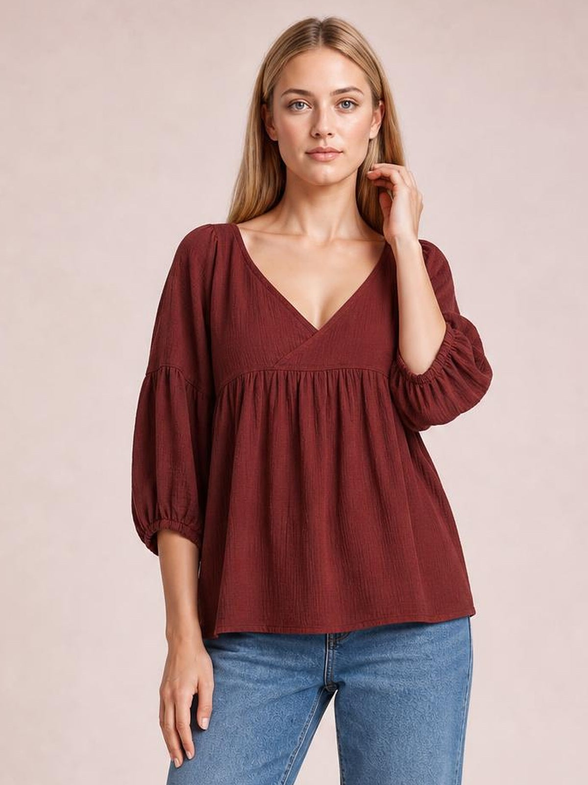 Model wears a solid burgundy dropped-shoulder V-neck blouse with a relaxed long silhouette, gathered waist seam, voluminous sleeves, and elastic cuffs.