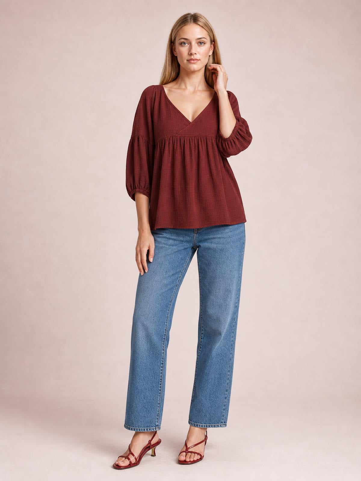 A model stands in a burgundy dropped-shoulder V-neck blouse with gathered long sleeves, a tiered seam, and a loose, flowing silhouette.
