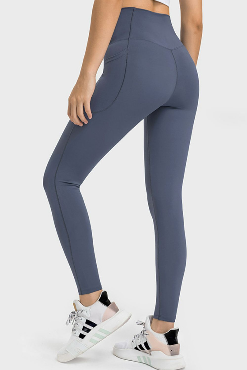 Model poses from the back in blue-gray V-waist yoga leggings with a side pocket, sculpting seams, a high-rise fit, and tapered full-length silhouette.