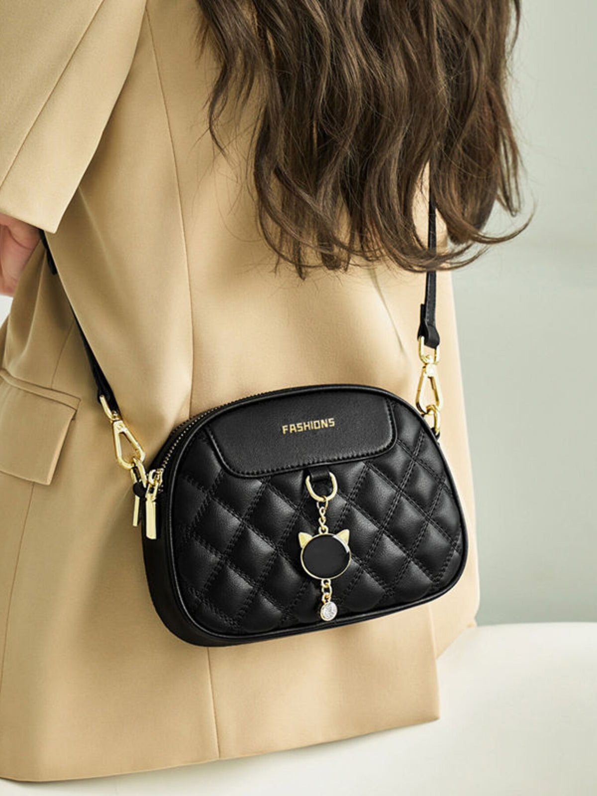 A model wears a black mini quilted PU leather crossbody bag with a rounded rectangular silhouette, zip top, gold-tone hardware, and decorative charm.
