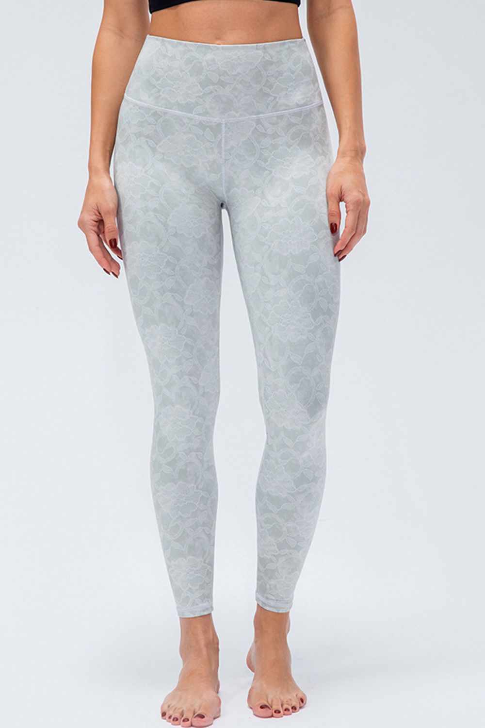 Model stands in light gray floral-print active leggings with a wide waistband, slim full-length silhouette, and visible front and curved waist seams.