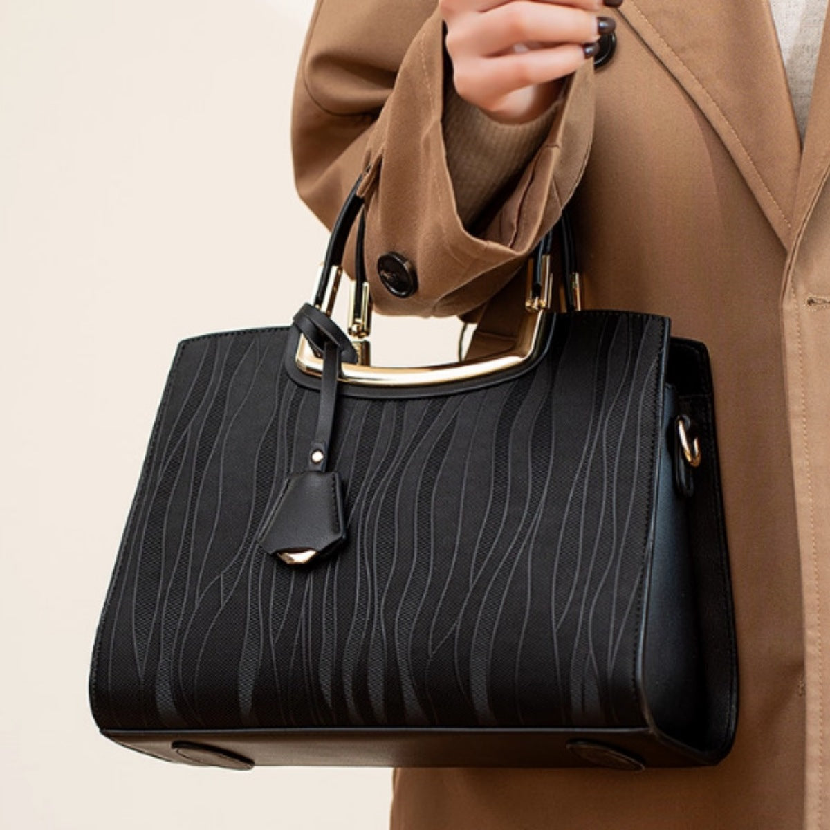 A model holds a medium black PU leather top-handle handbag with a structured silhouette, embossed texture, gold-tone frame hardware, and a hanging tag.