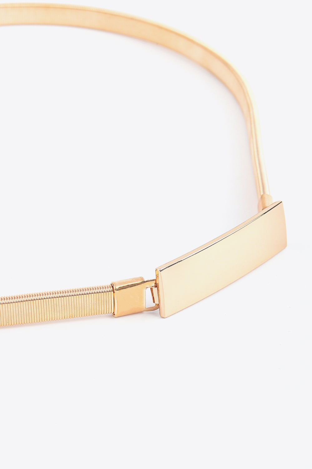 Close-up of a slender elastic iron belt in a warm metallic finish, featuring a structured rectangular buckle and ribbed stretch construction.