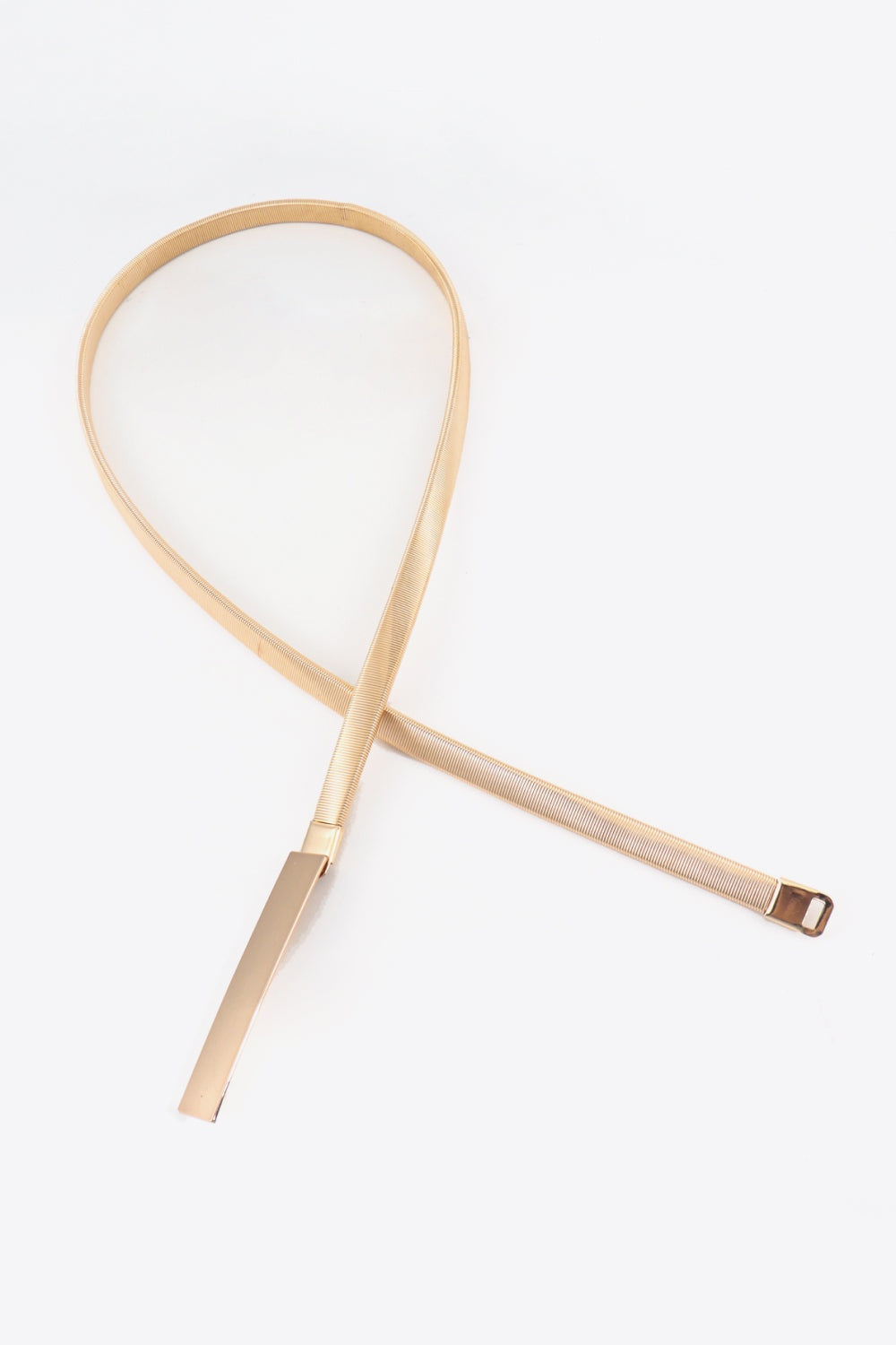 A slender champagne-metallic elastic iron belt lies flat, featuring a sleek profile and elongated rectangular buckle for polished waist definition.