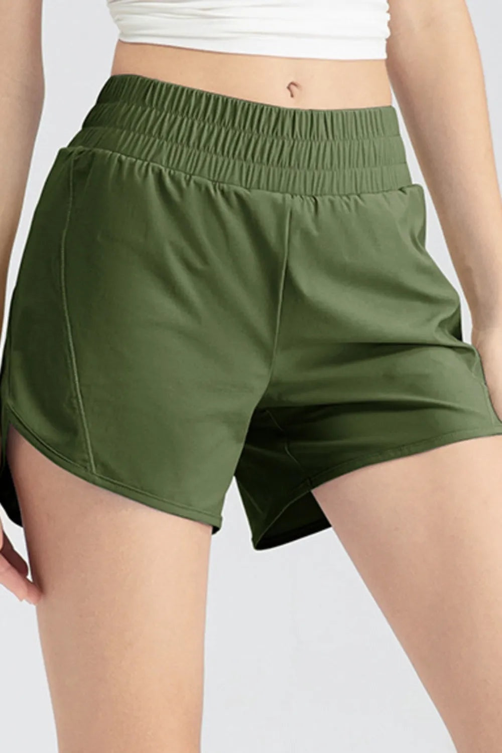 Model wearing olive green elastic waist active shorts with a relaxed, loose silhouette, curved hems, and visible stitched side seams.