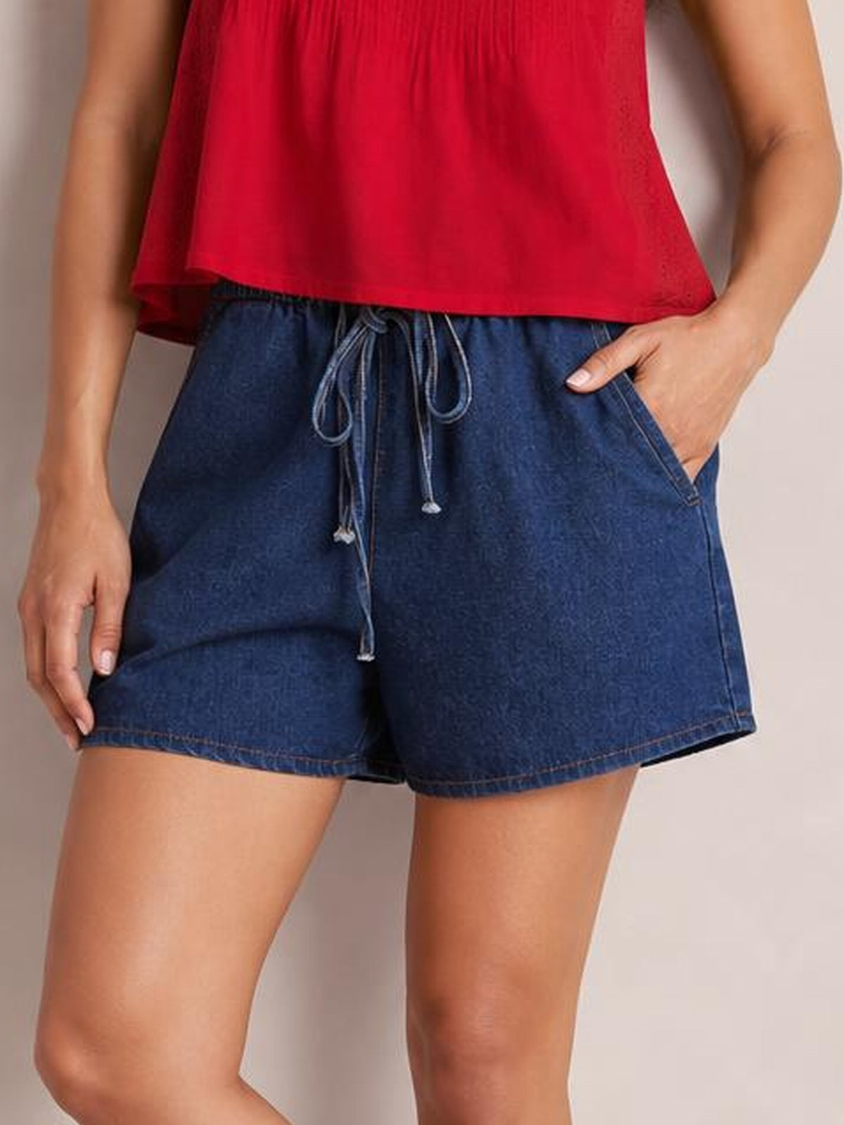 Model wearing dark blue elastic waist denim shorts with a tied drawstring, slanted side pockets, relaxed silhouette, and neatly stitched hems.
