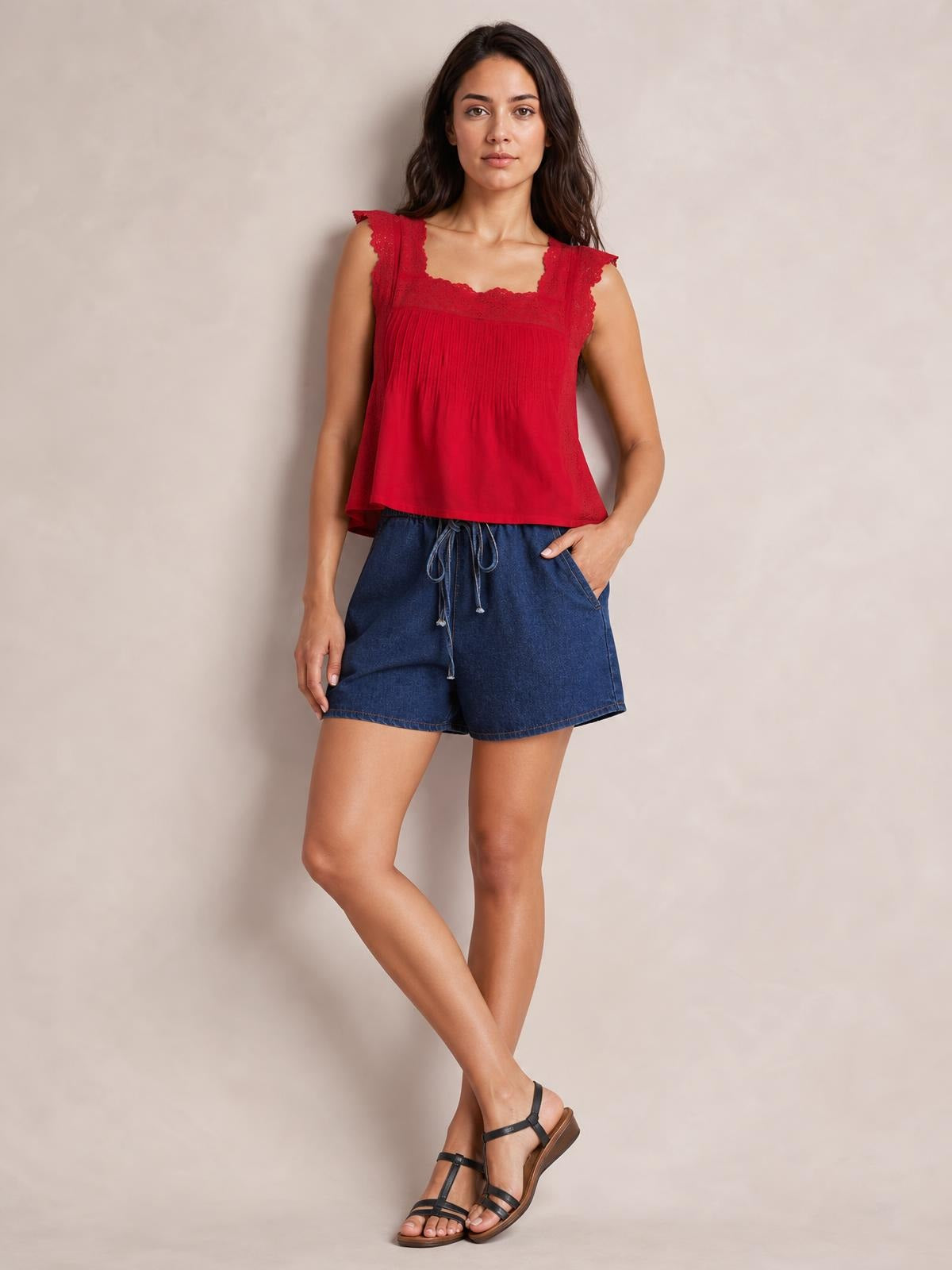 A model poses with one hand in a pocket, wearing dark blue denim shorts with an elastic waist, front tie detail, and relaxed straight-leg silhouette.
