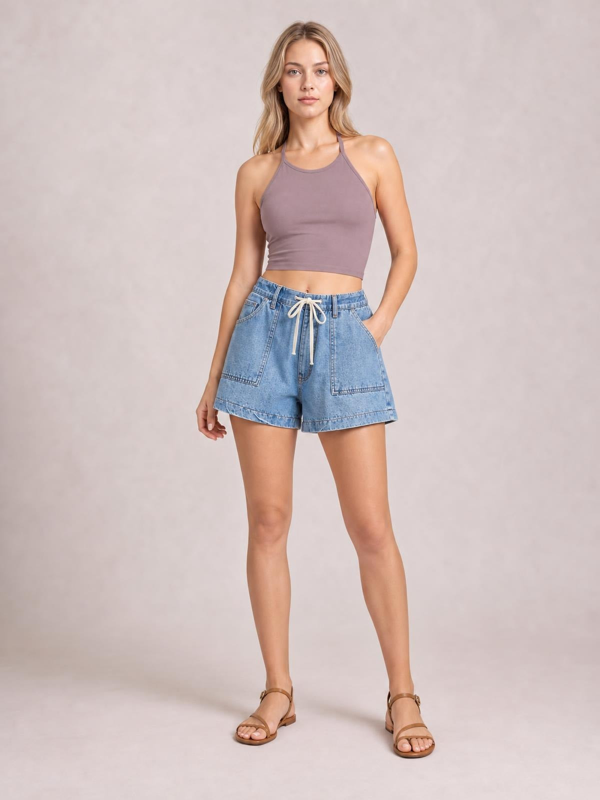 A model poses in light blue elastic waist denim shorts with a drawstring, large front pockets, belt loops, and a relaxed straight-leg silhouette.