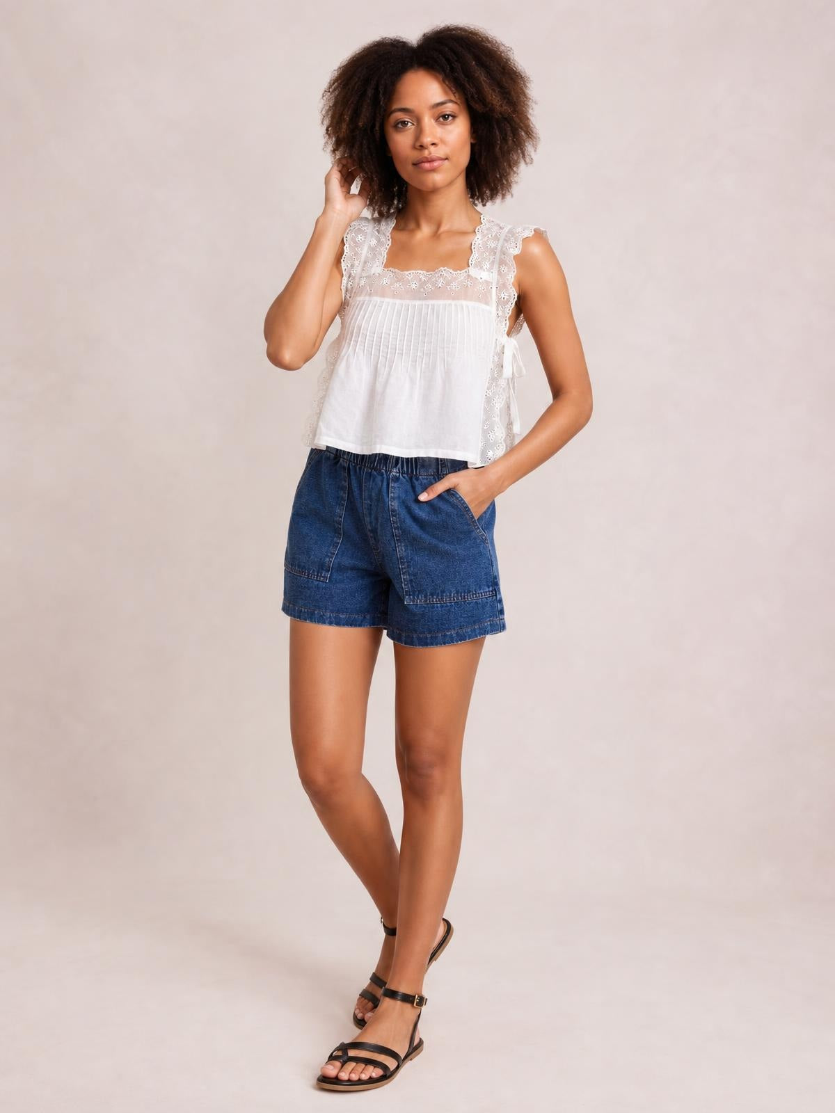 Model poses in dark blue elastic-waist denim shorts with a drawstring, roomy patch pockets, and a relaxed straight-leg silhouette.
