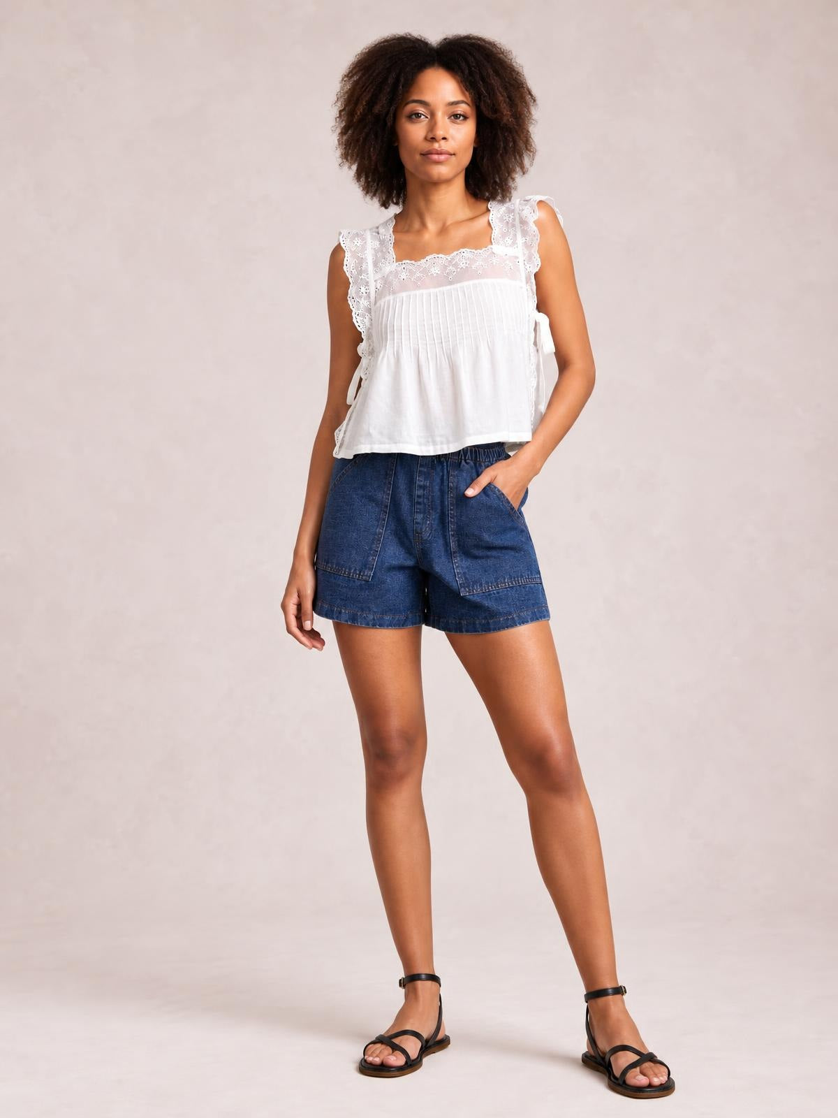 A model poses in dark blue elastic waist denim shorts with a relaxed silhouette, front patch pockets, and a straight hem, one hand tucked into a pocket.