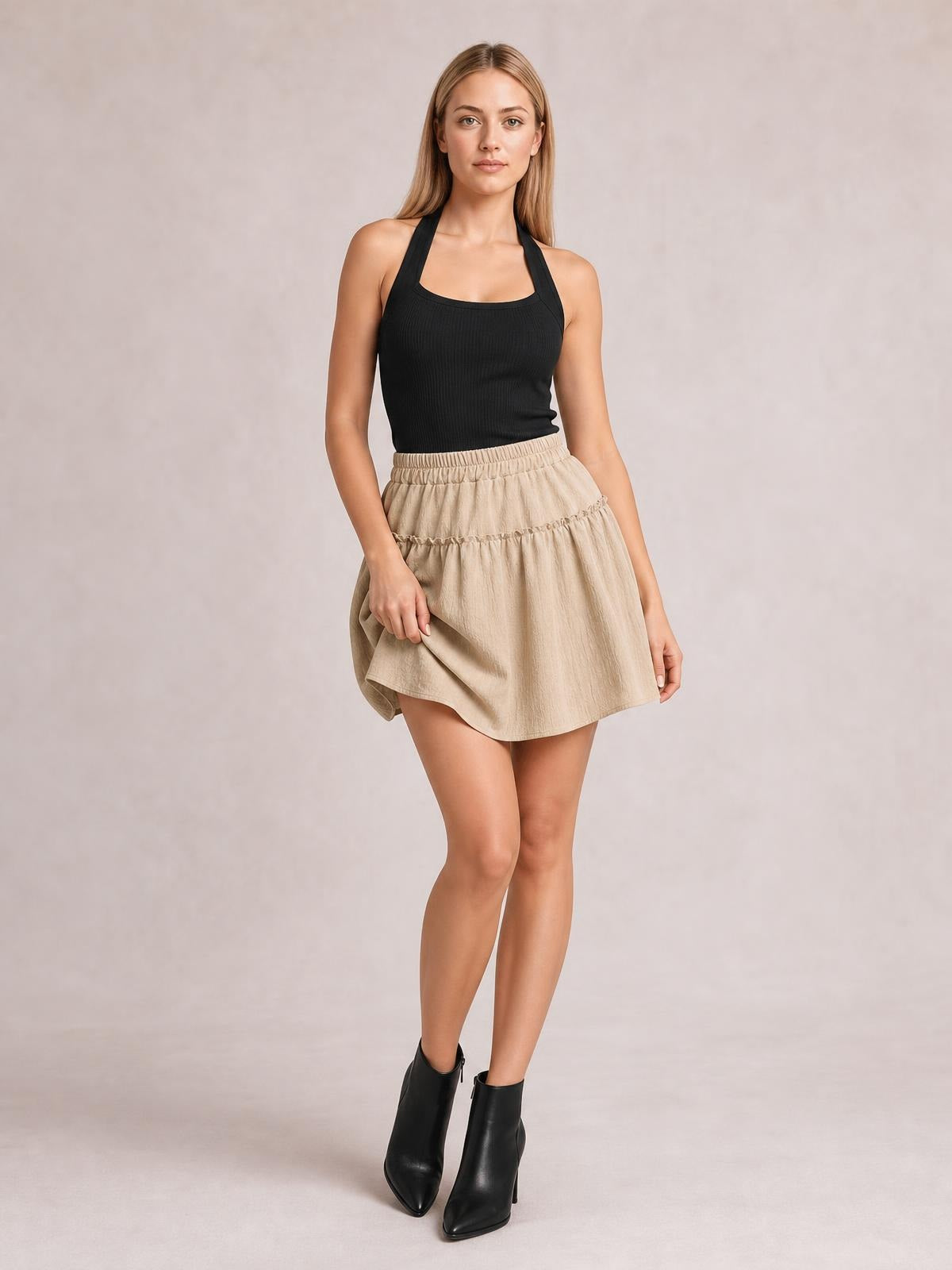 Model poses in a beige elastic waist layered skirt with frill tiers and a flowy A-line silhouette, gently lifting the hem.