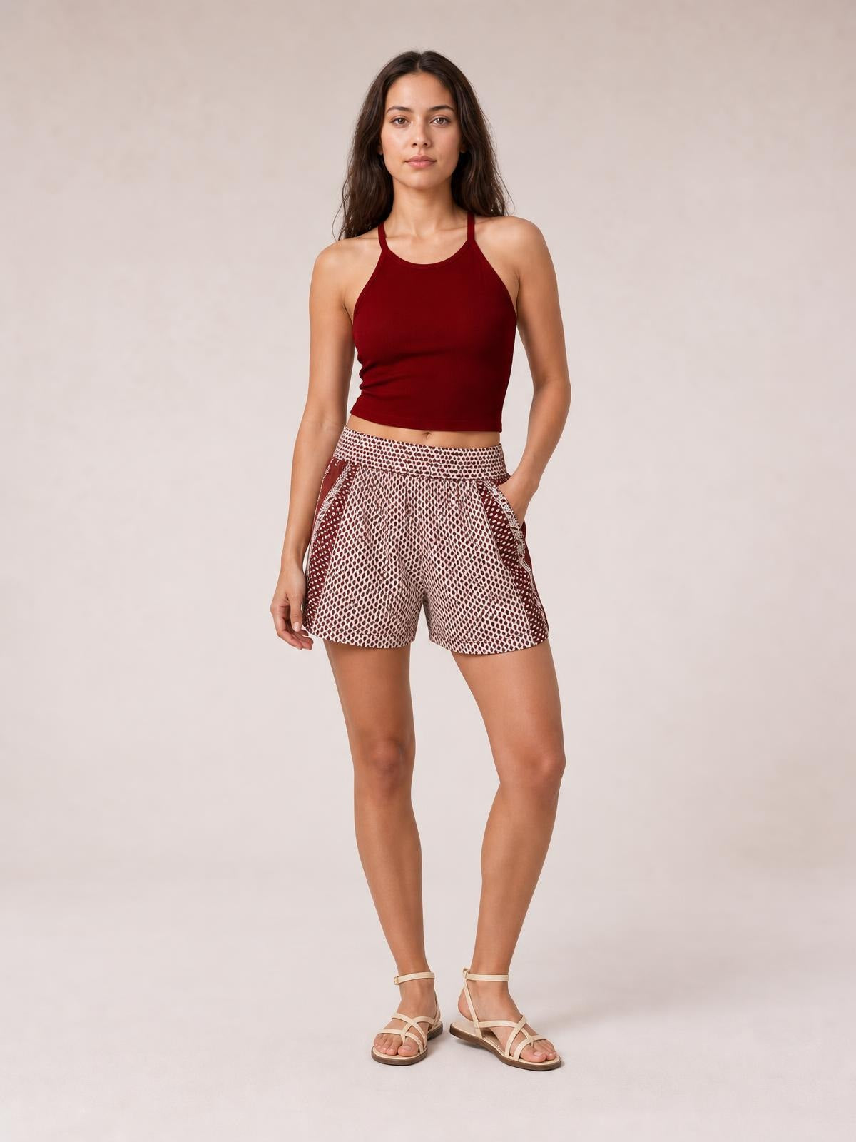 Model wears patterned brown and cream elastic waist shorts with a relaxed silhouette, angled side pockets, and a mid-thigh hem while standing with one hand in a pocket.