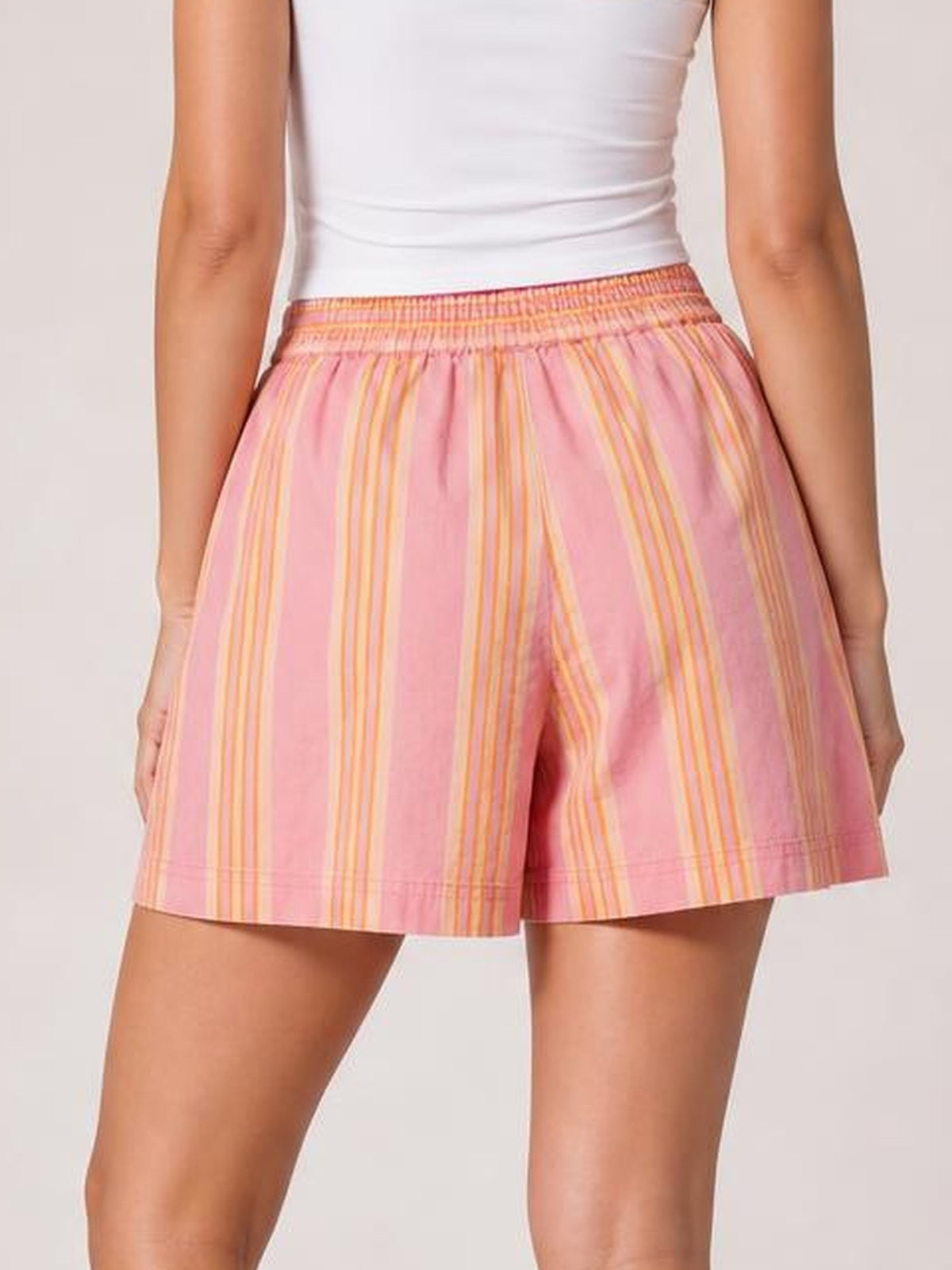 A model wears pink and yellow striped elastic waist shorts with a relaxed silhouette, gathered waistband, straight hems, and convenient side pockets.