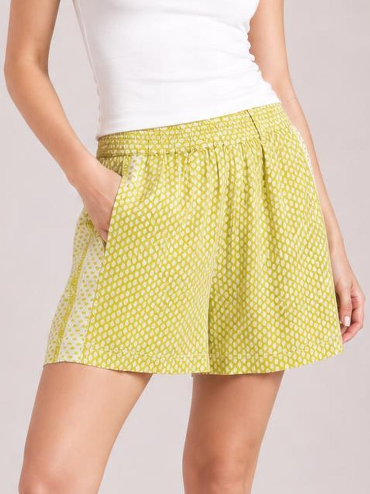 Model wearing lime green patterned elastic waist shorts with a relaxed, flared silhouette, front pockets, and a visible center seam.