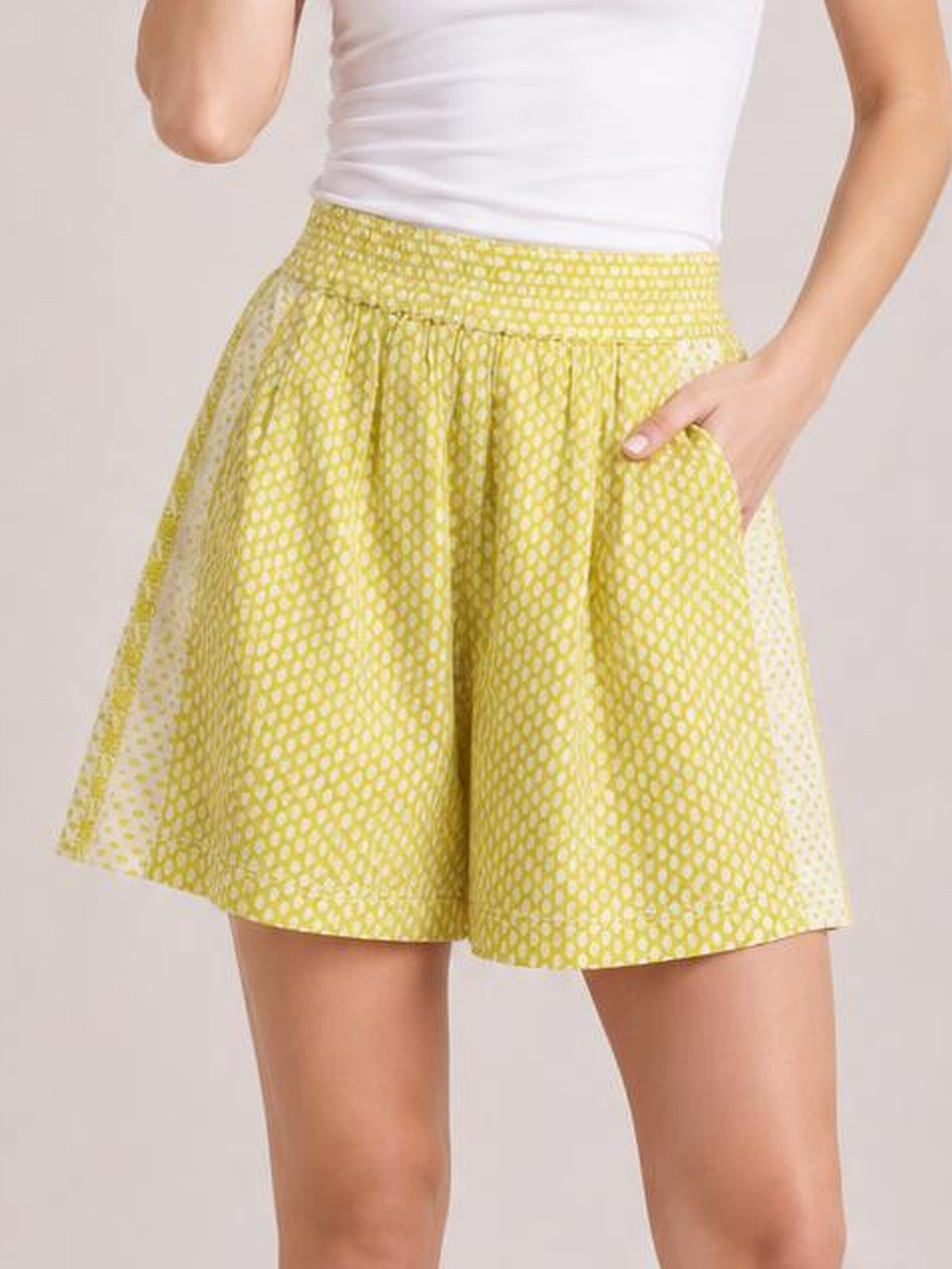 A model wears yellow-green patterned elastic waist shorts with a gathered waistband, relaxed wide-leg silhouette, and convenient side pockets, posing with one hand inside.