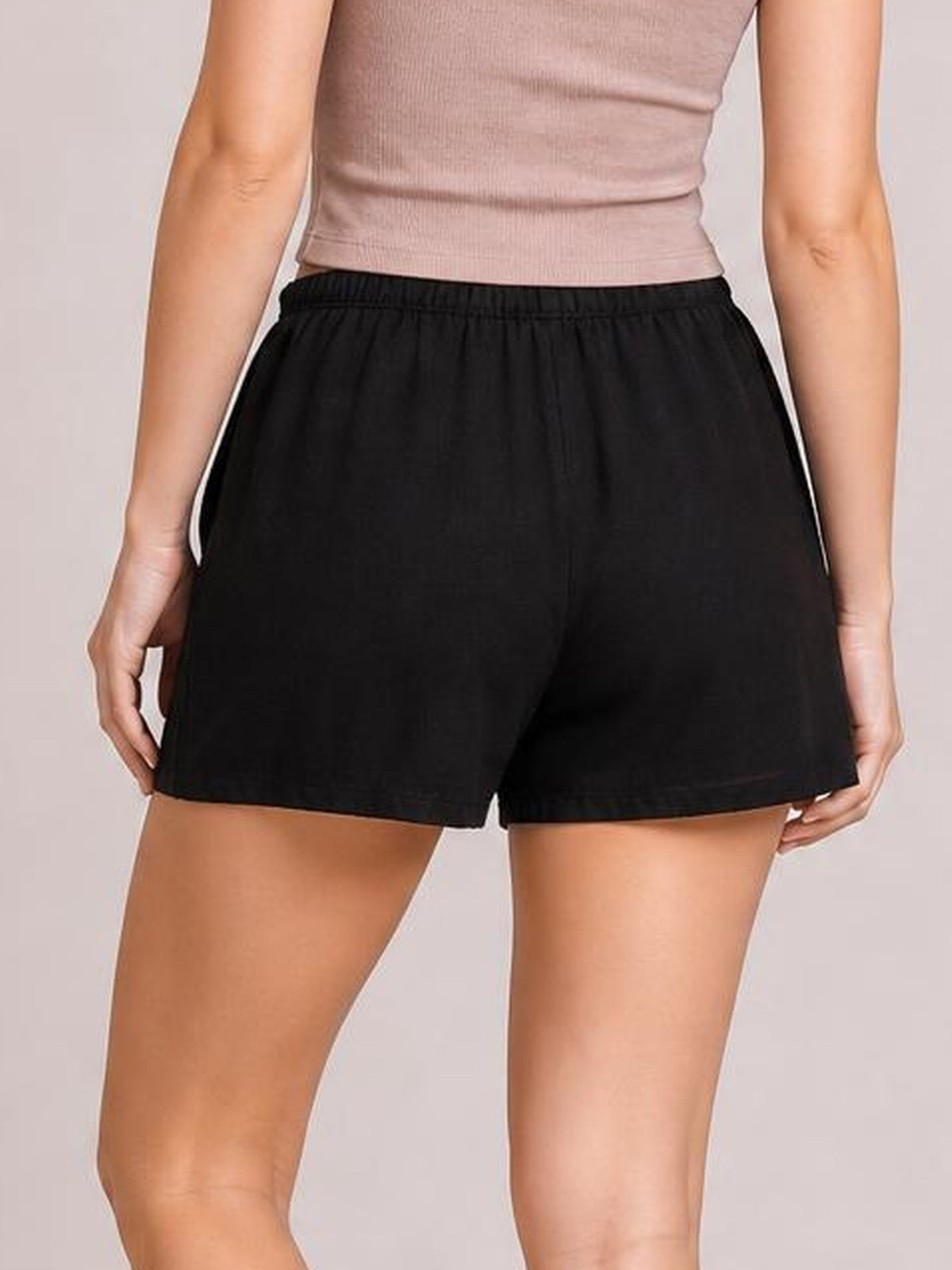 Model shown from behind wearing black elastic waist shorts with a relaxed straight-leg silhouette, side pockets, and cleanly finished hems.
