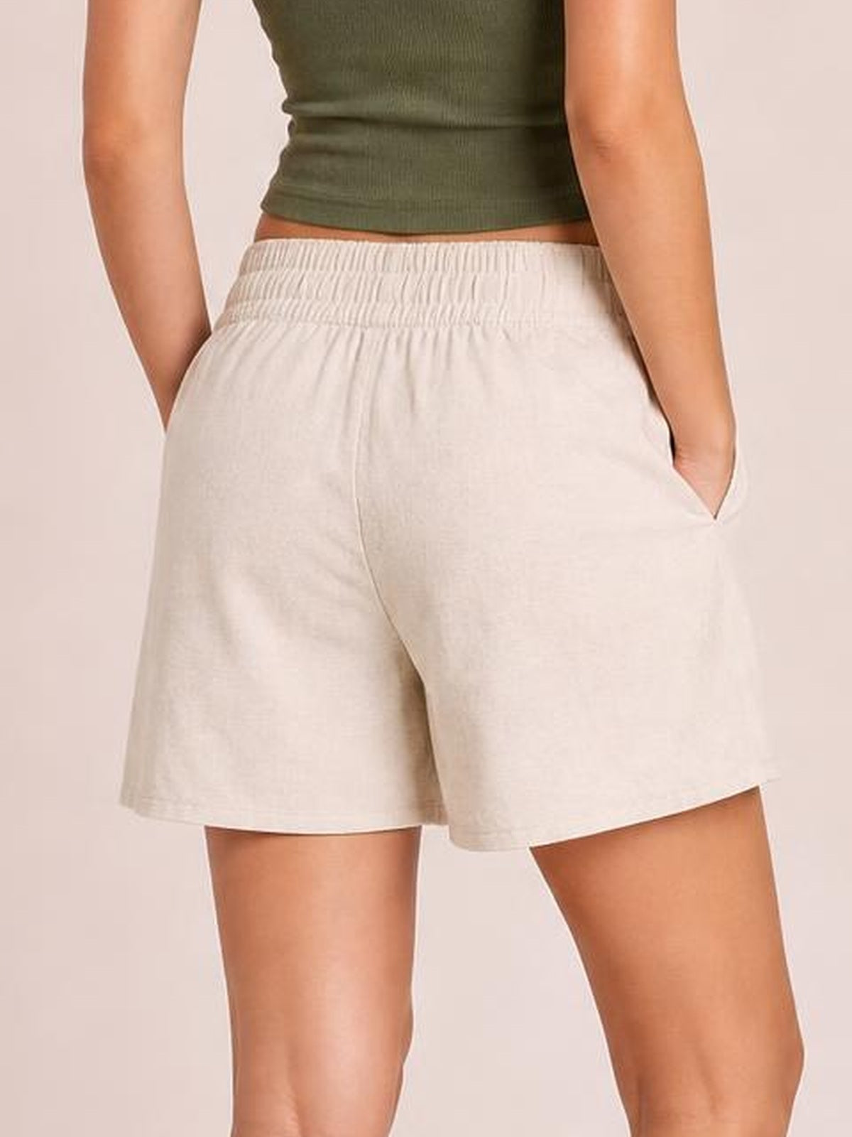 Model wears cream elastic waist shorts with a relaxed, straight-leg silhouette, visible side pockets, and hands tucked into the pockets.