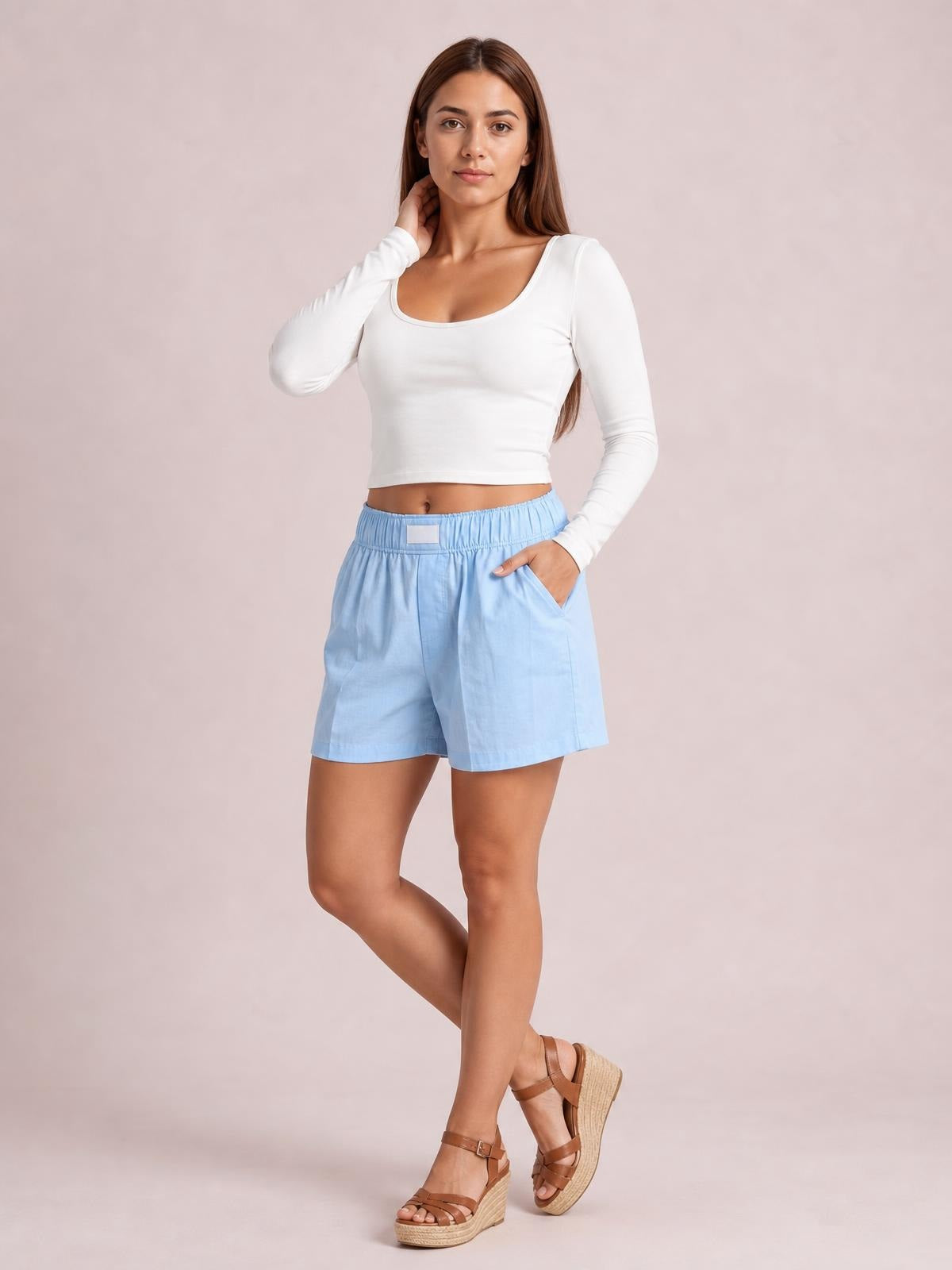 Model poses in light blue elastic waist shorts with a relaxed straight-leg silhouette, front pockets, and a smooth waistband.