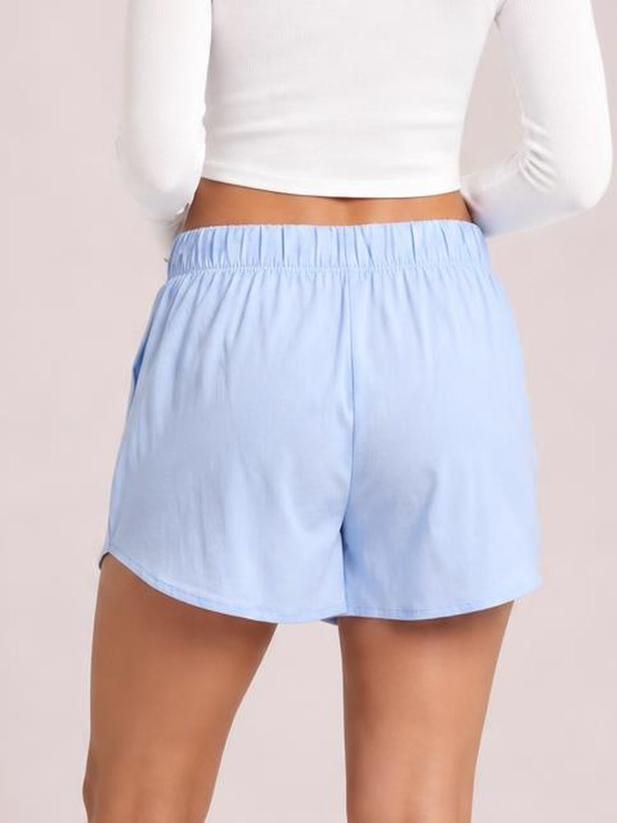 Model shown from the waist down wears light blue elastic waist shorts with a relaxed silhouette, side pockets, gathered waistband, and curved hems.