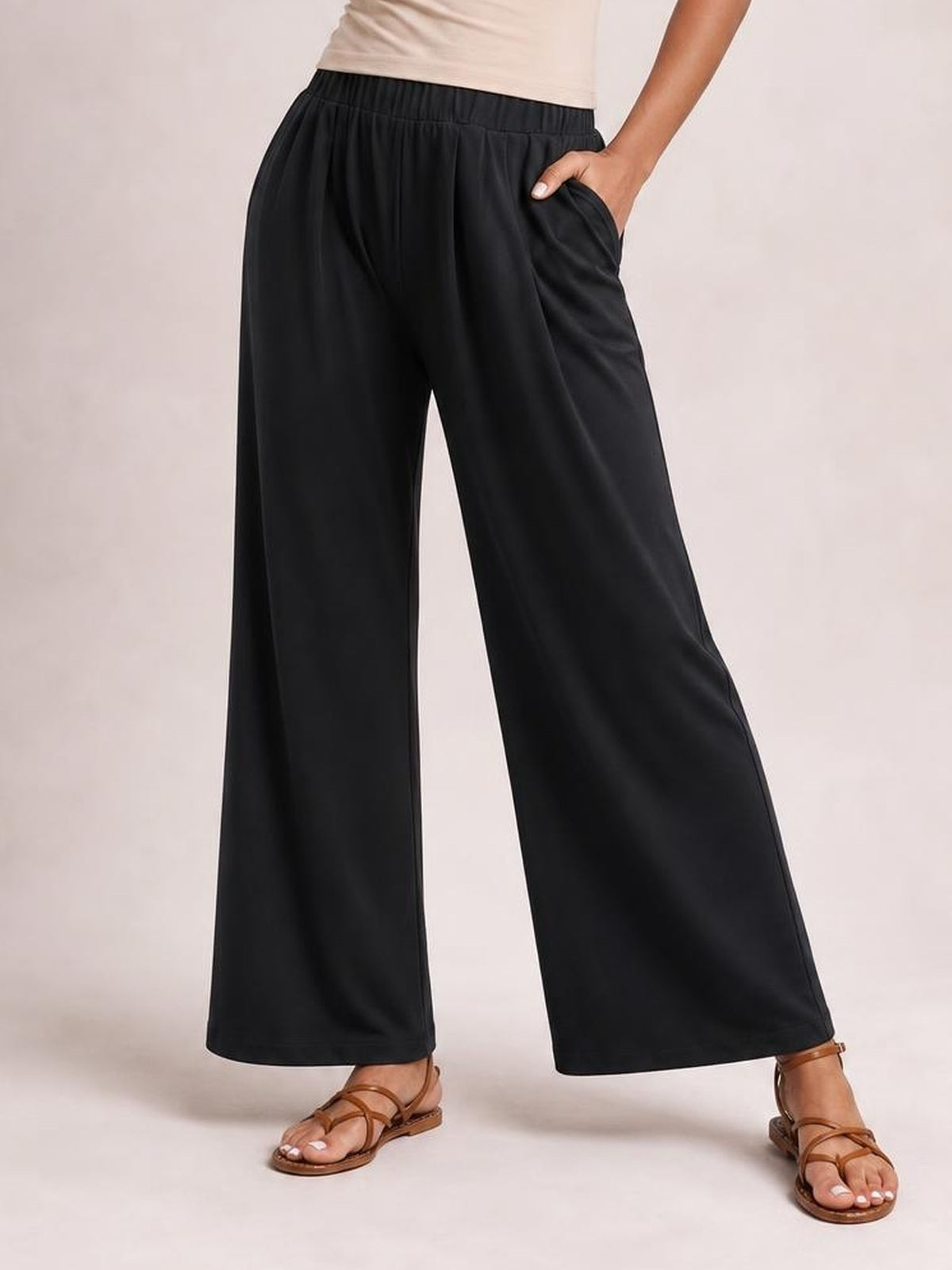 A model poses in black elastic waist wide leg pants with a flowing silhouette, side pockets, and one hand tucked into a pocket.