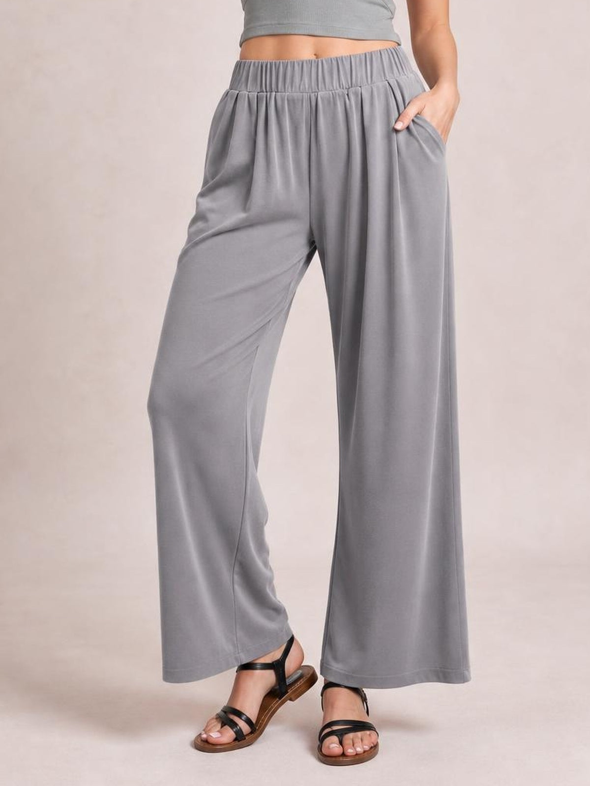 A model wears gray elastic waist wide leg pants with a relaxed silhouette, flowing full-length legs, and side pockets, posing with one hand tucked inside.
