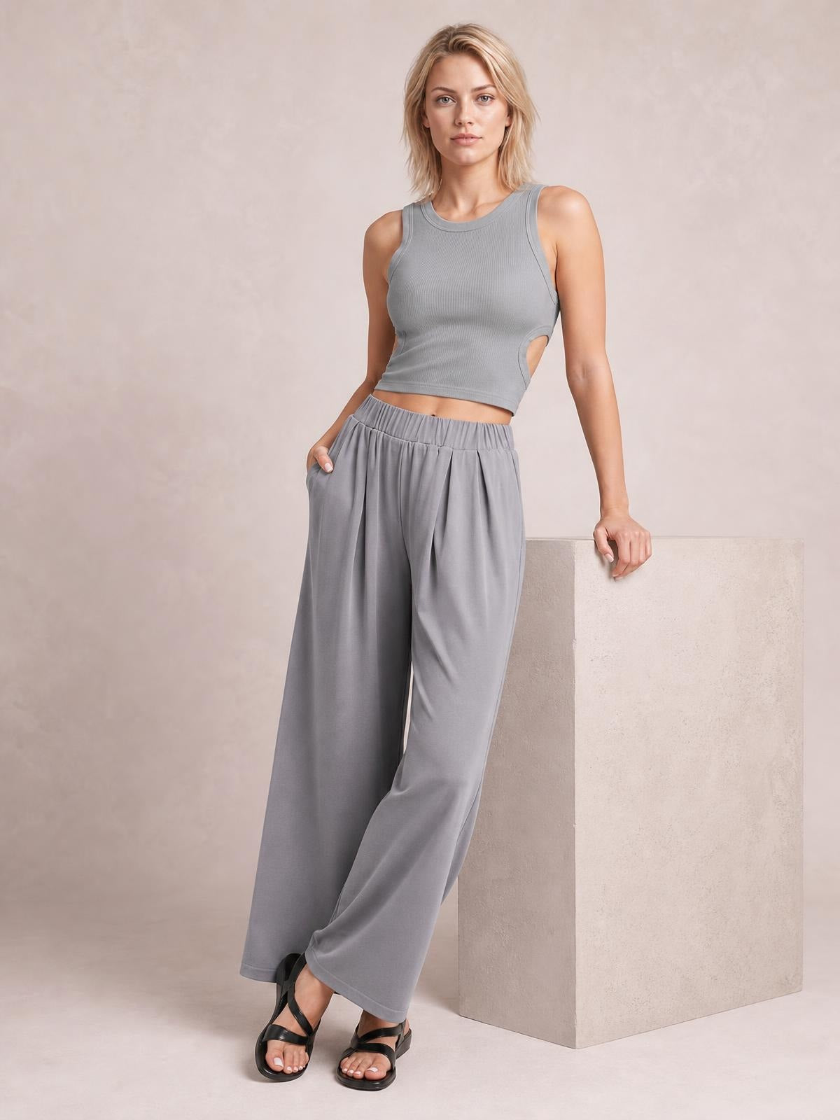 Model wearing gray elastic waist wide leg pants with a relaxed flowing silhouette and side pockets, standing with one hand in a pocket.