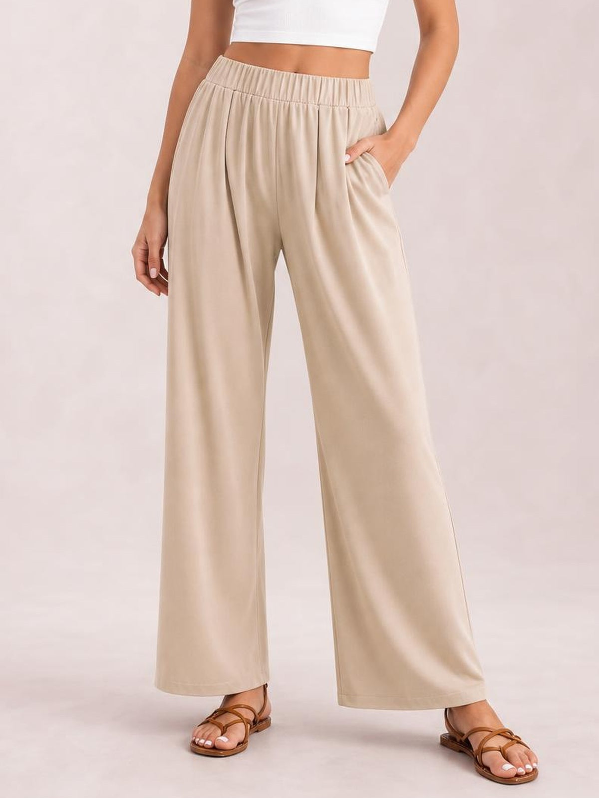 A model stands in beige elastic waist wide leg pants with a relaxed silhouette, visible side pockets, and softly draped construction.