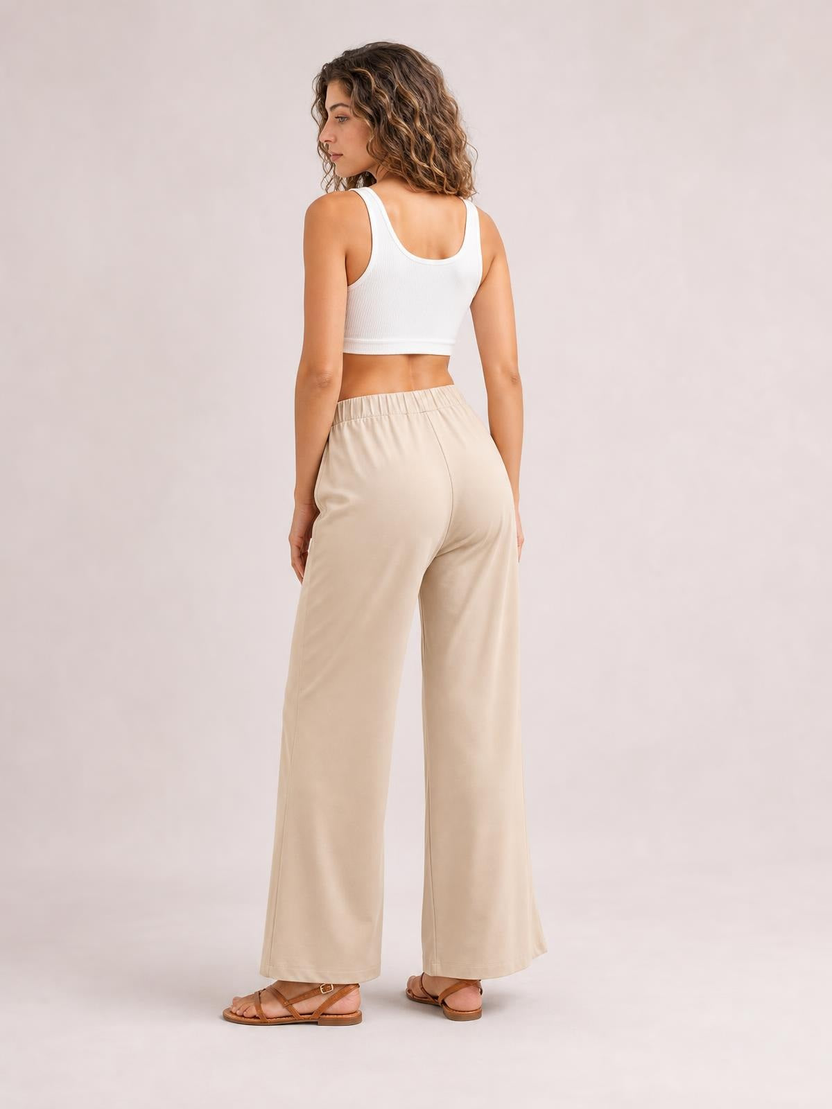 Model shown from behind wearing beige elastic-waist wide-leg pants with a relaxed, full-length silhouette and smooth construction.