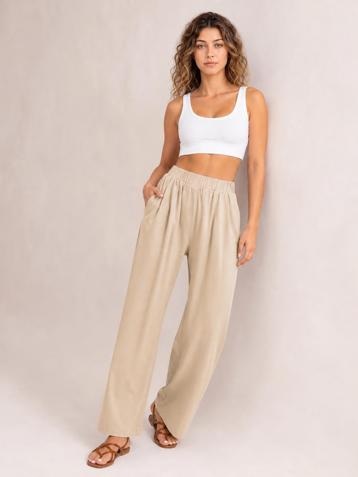 Model poses in beige elastic waist wide leg pants with a relaxed silhouette, visible side pockets, and softly gathered construction.