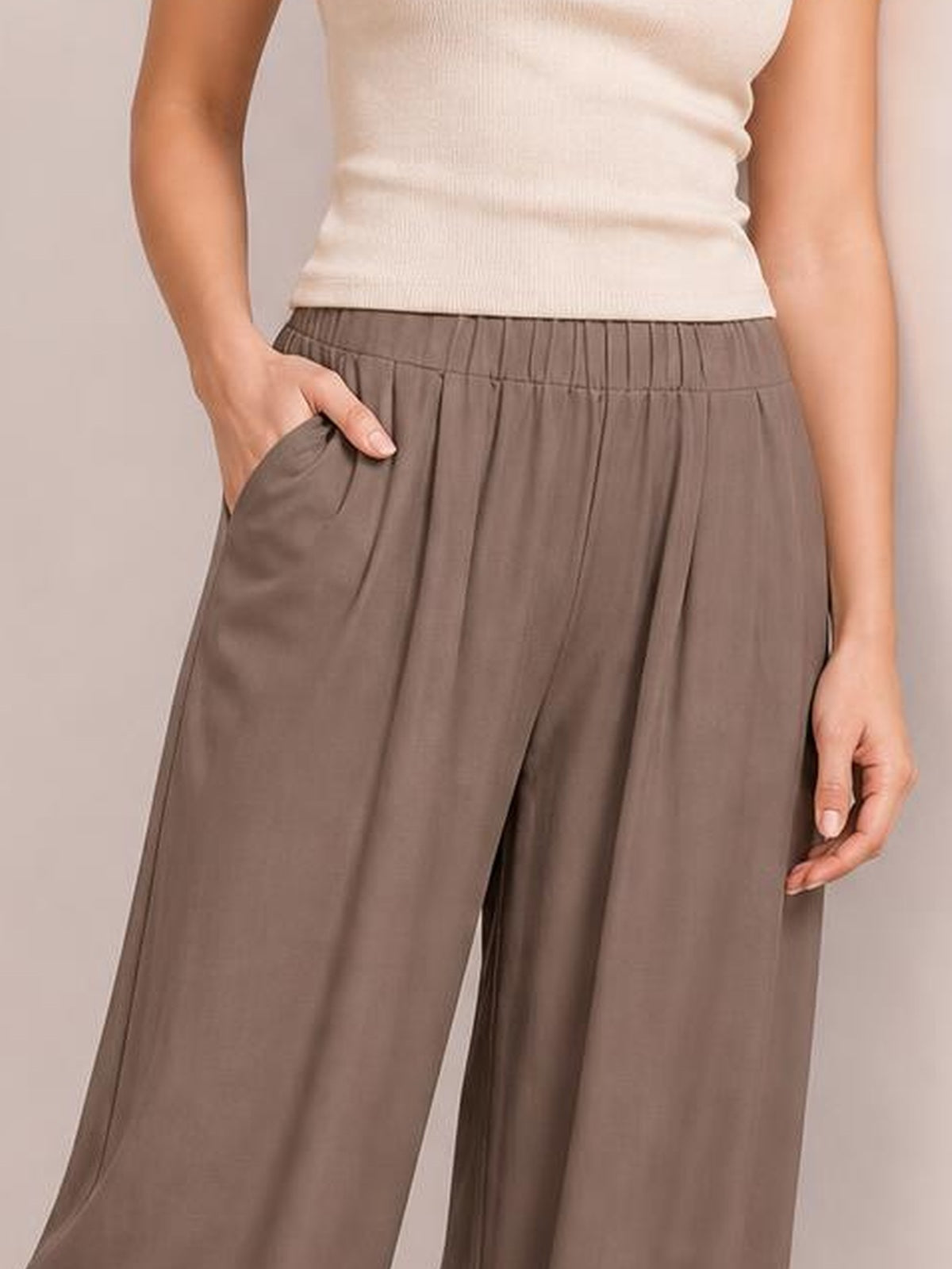 Model wearing taupe elastic waist wide leg pants with front pockets, a flowing silhouette, and visible vertical seam detailing.