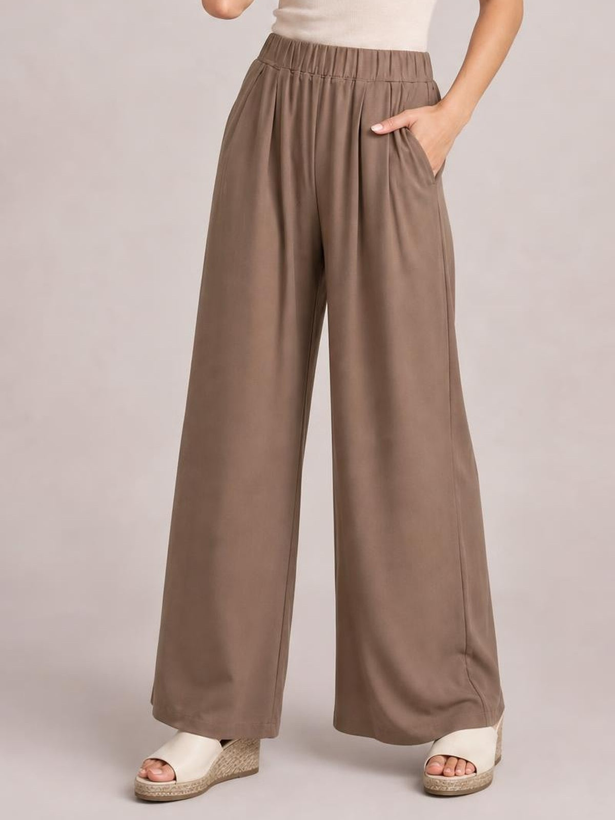 Model wearing taupe elastic waist wide leg pants with a flowing full-length silhouette, visible side pockets, and softly gathered waistband.