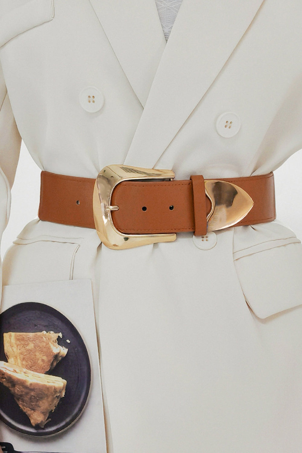 A model wears a wide brown PU belt over a white blazer, cinched at the waist with a polished gold-tone buckle, keeper loop, and visible perforations.