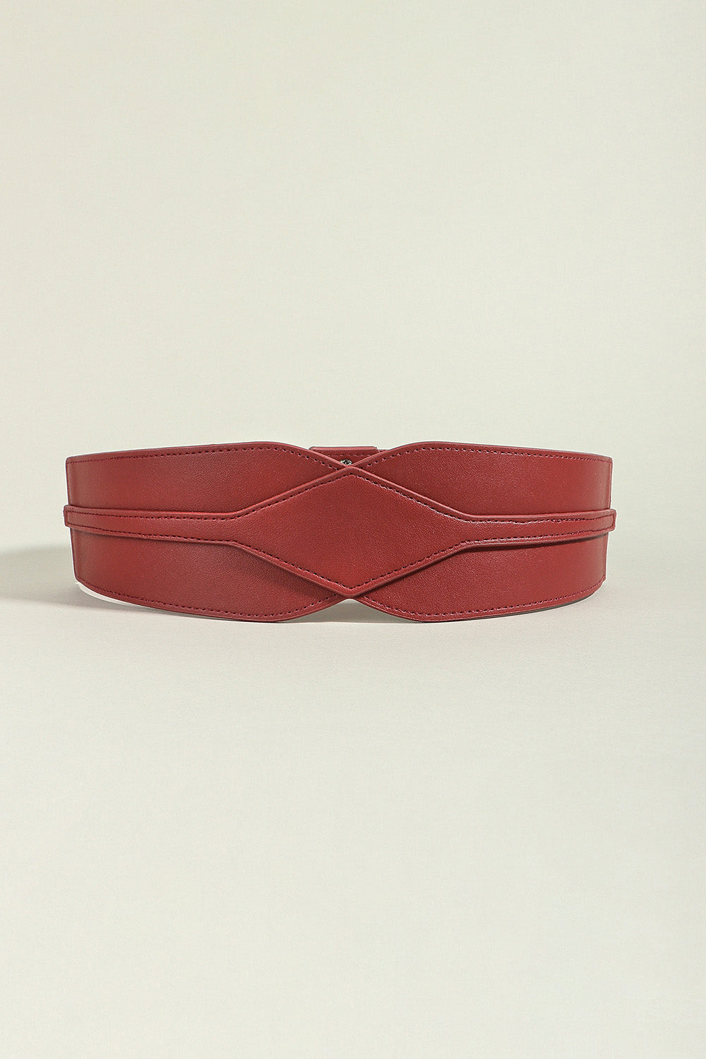 Burgundy elastic wide PU belt with a broad sculptural silhouette, smooth finish, stitched edges, and a contoured crossed front design.